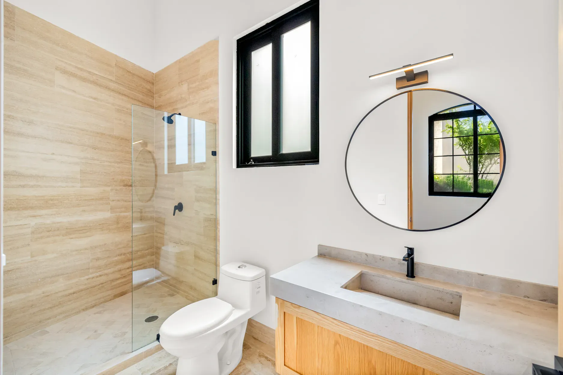 Casa Ronda, bathroom with a travertine shower, a round black mirror, a wood vanity and a toilet, San Miguel de Allende