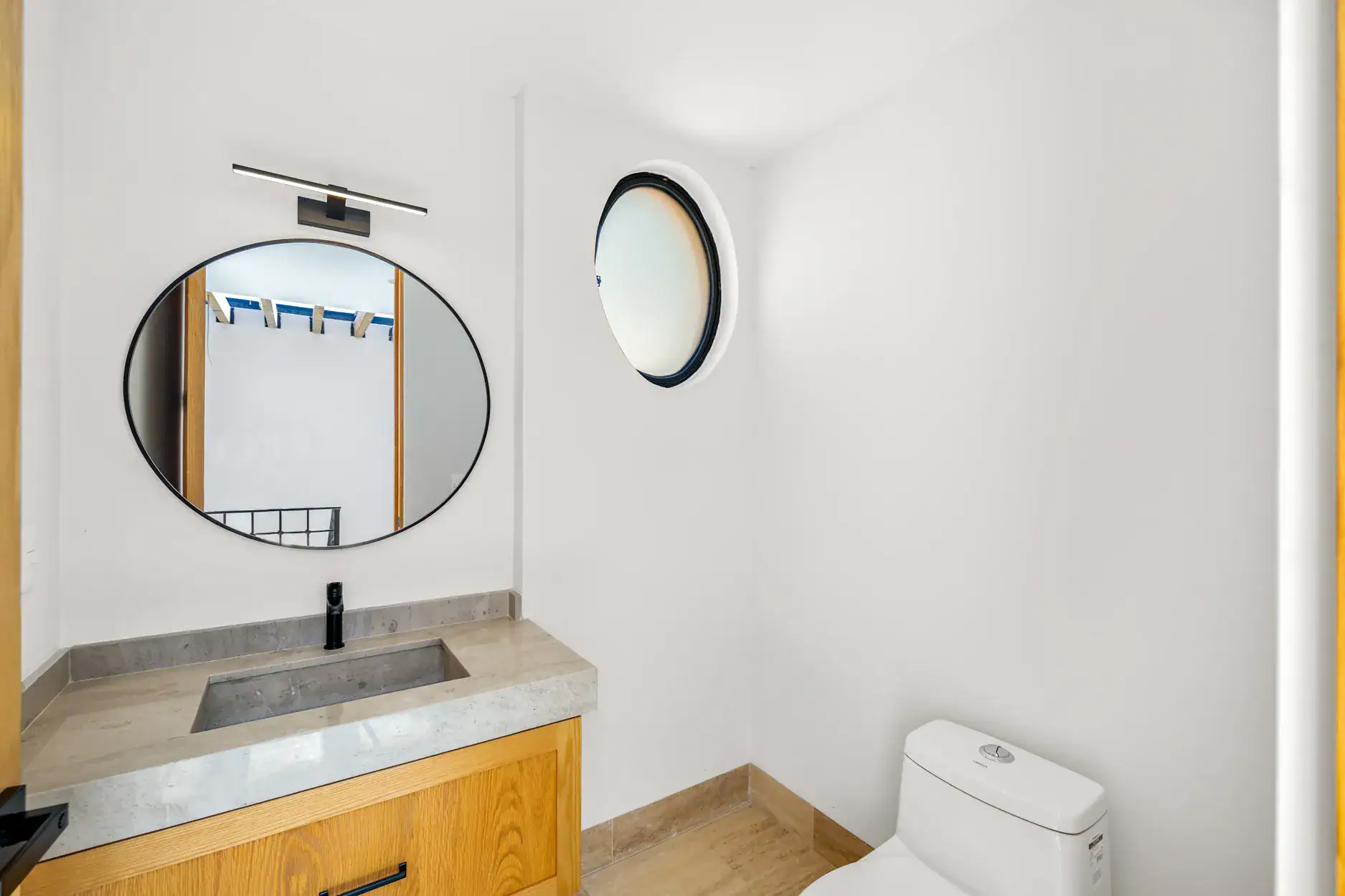 Casa Ronda, powder room with a round mirror, a stone sink, a round window and a toilet, San Miguel de Allende