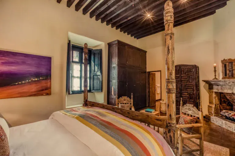 Casa San Jose, primary bedroom with a carved four-poster bed and striped blanket, San Miguel de Allende