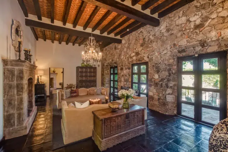 Casa San Jose, living area with a stone wall, chandelier and wood beam ceiling, San Miguel de Allende