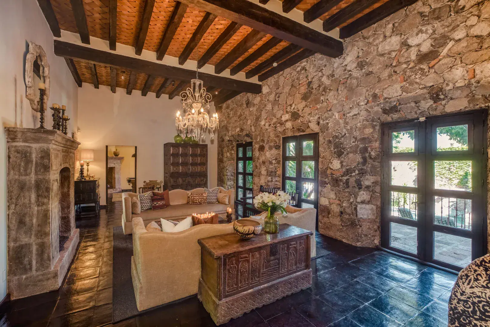Casa San Jose, living area with a stone wall, chandelier and wood beam ceiling, San Miguel de Allende