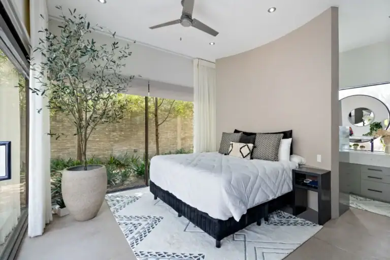 Casa Sanchez Renero, bedroom with a curved wall, a white bed and floor-to-ceiling glass to a planted courtyard, San Miguel de Allende