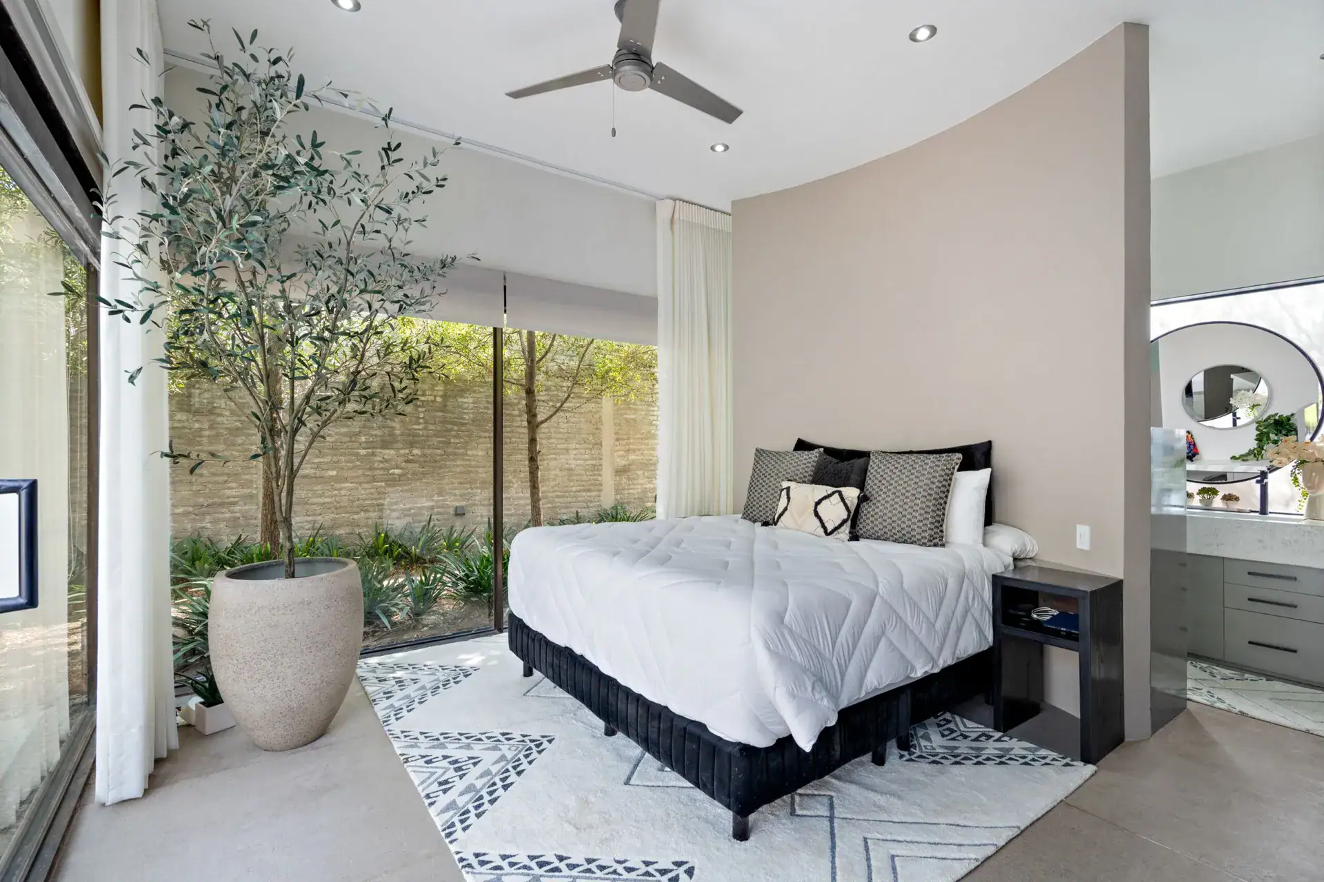 Casa Sanchez Renero, bedroom with a curved wall, a white bed and floor-to-ceiling glass to a planted courtyard, San Miguel de Allende