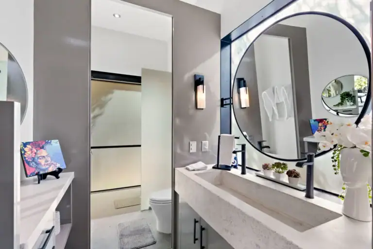 Casa Sanchez Renero, bathroom with a round black-framed mirror, a stone trough sink and black fixtures, San Miguel de Allende