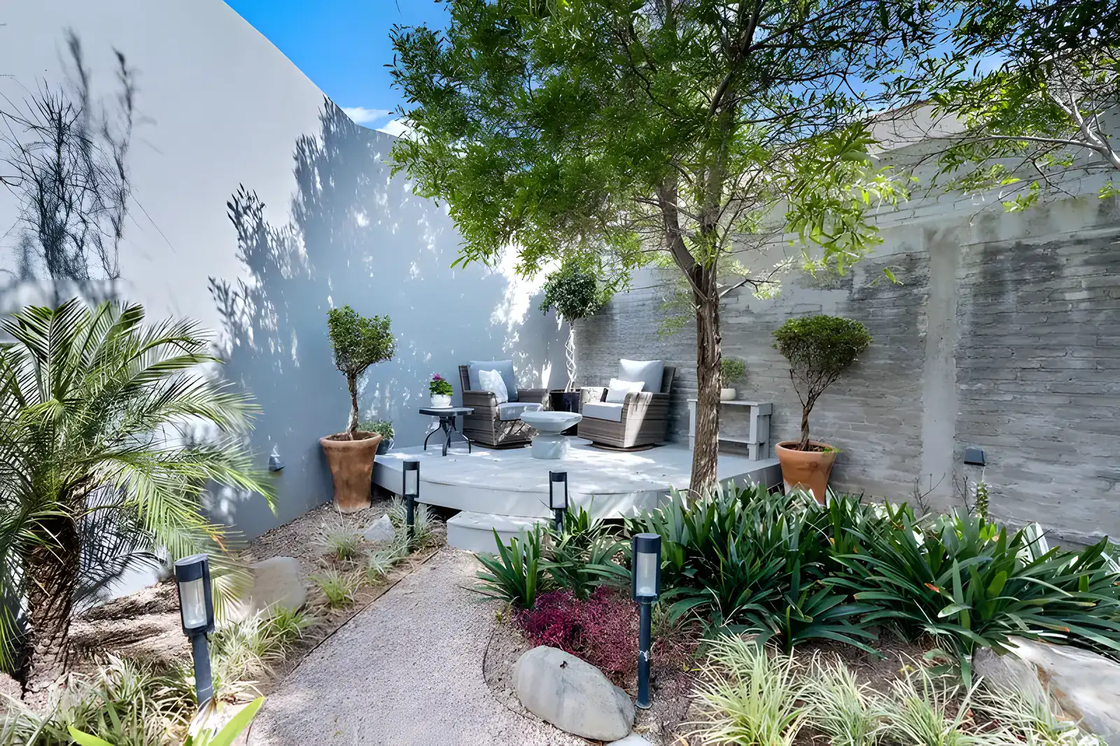 Casa Sanchez Renero, garden patio with a lounge area on a wood deck under a tree and palms, San Miguel de Allende