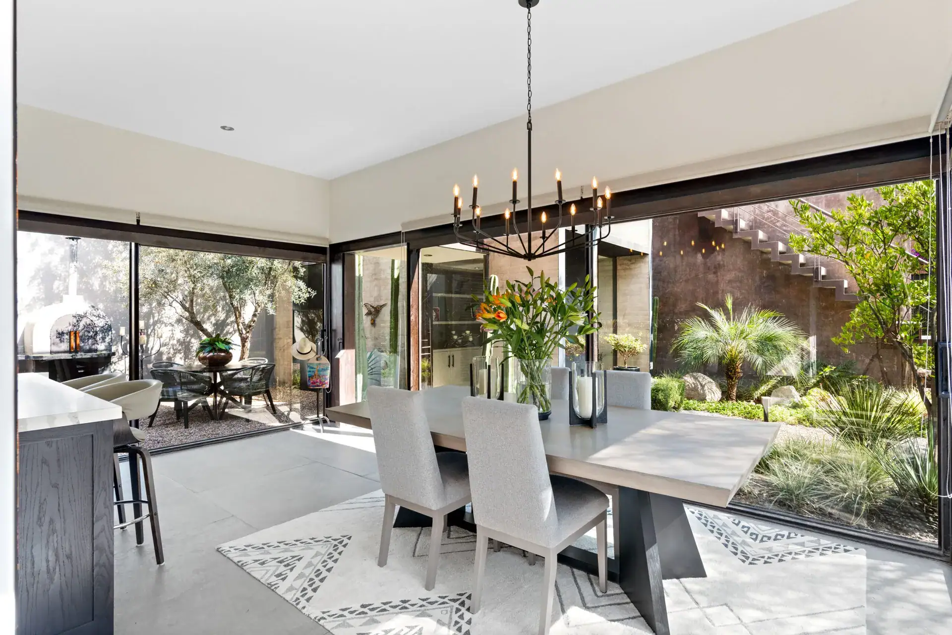 Casa Sanchez Renero, dining area with a gray table, upholstered chairs, an iron chandelier and a glass corner wall to the garden, San Miguel de Allende