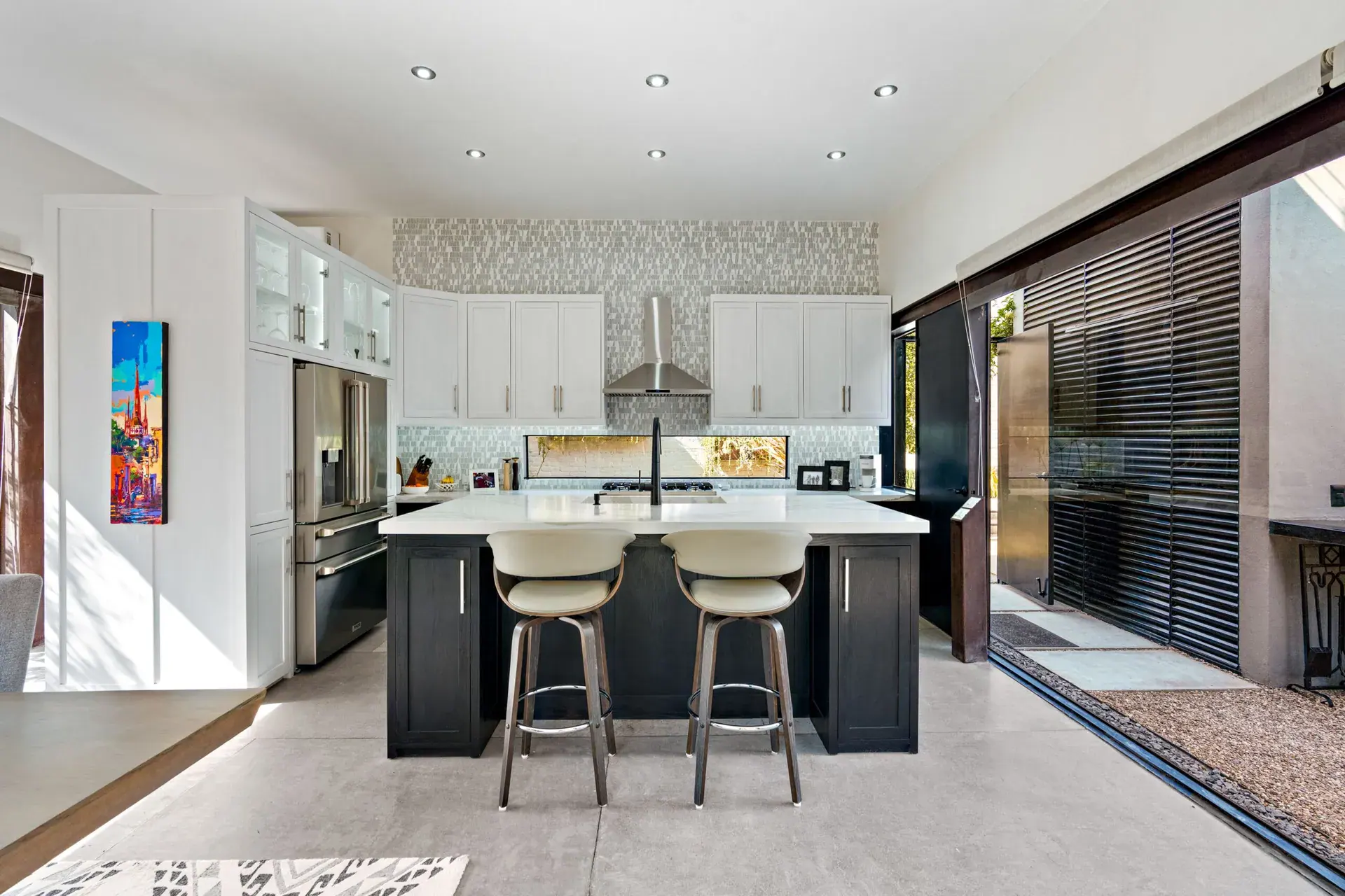 Casa Sanchez Renero, kitchen with a white and navy island, cream bar stools, white cabinets and a mosaic backsplash, San Miguel de Allende