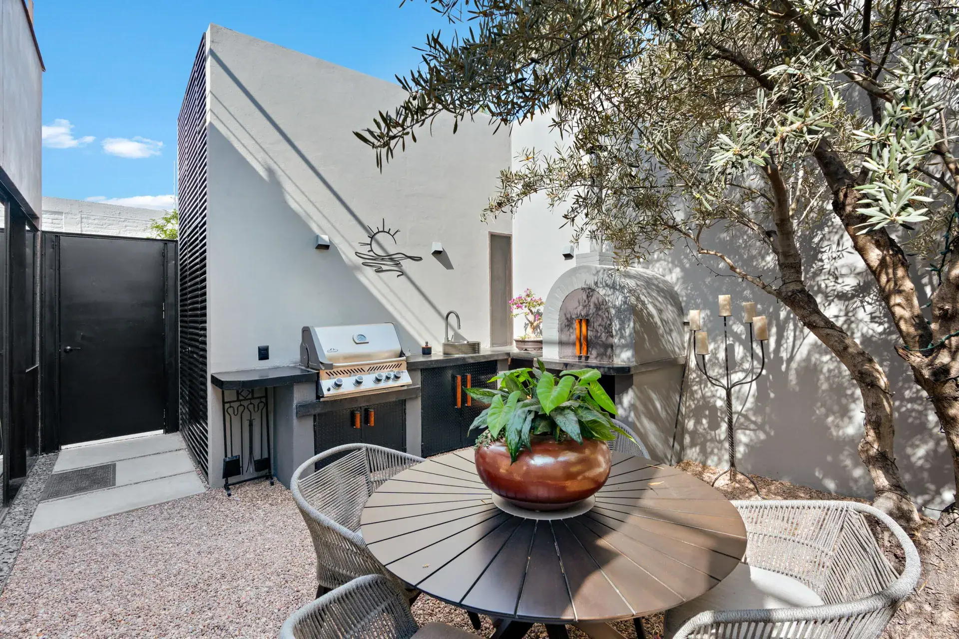 Casa Sanchez Renero, outdoor kitchen with a grill, a round table with woven chairs and a decorative bird sculpture, San Miguel de Allende
