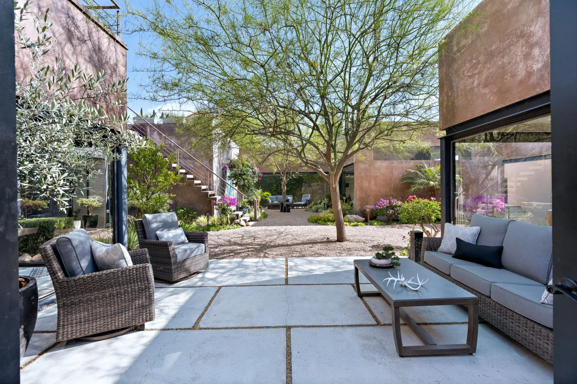 Casa Sanchez Renero, courtyard lounge with wicker chairs and a sofa on concrete pavers under a mature tree, San Miguel de Allende