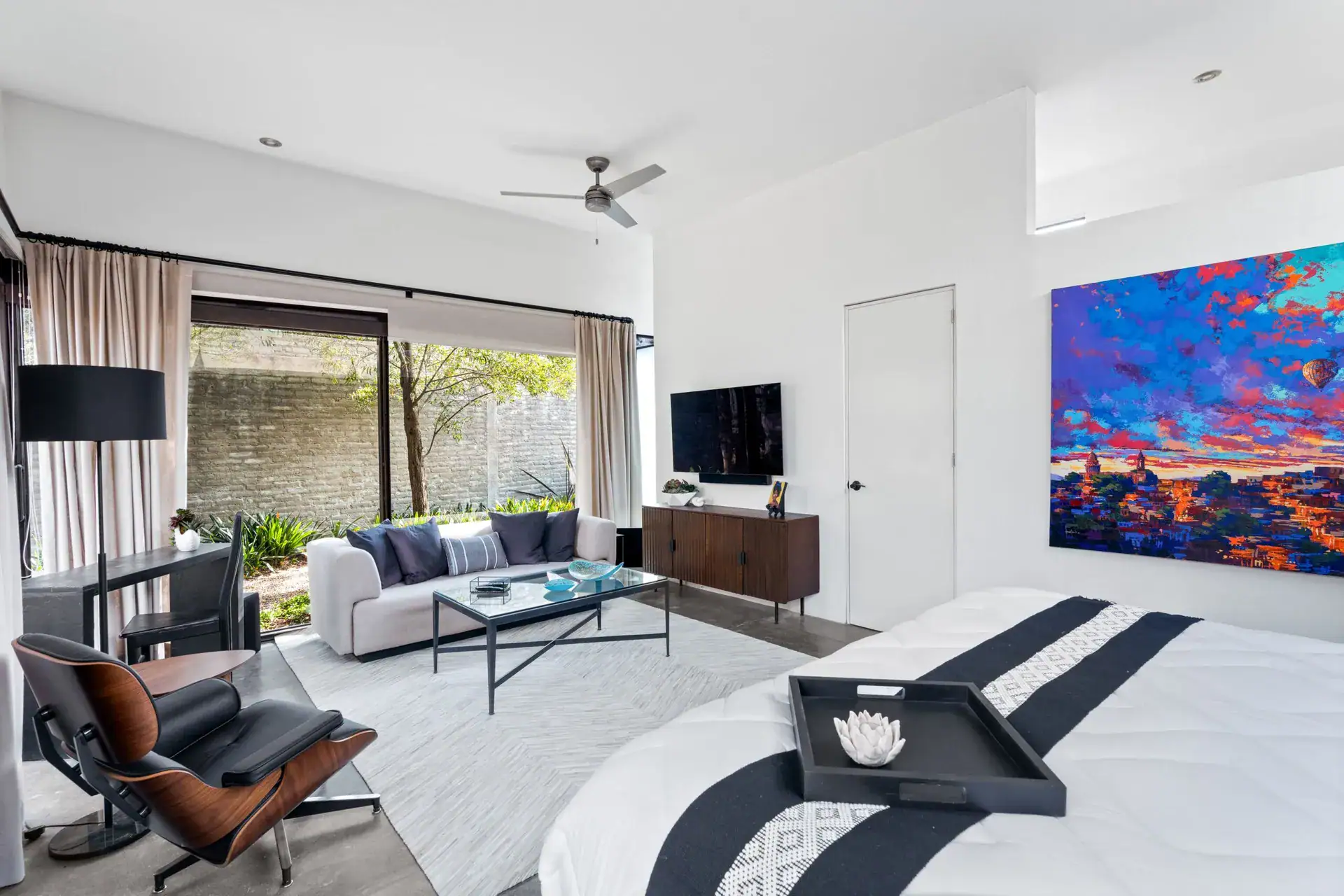 Casa Sanchez Renero, bedroom with a leather lounge chair, a sofa, a large colorful painting and a glass wall to the patio, San Miguel de Allende