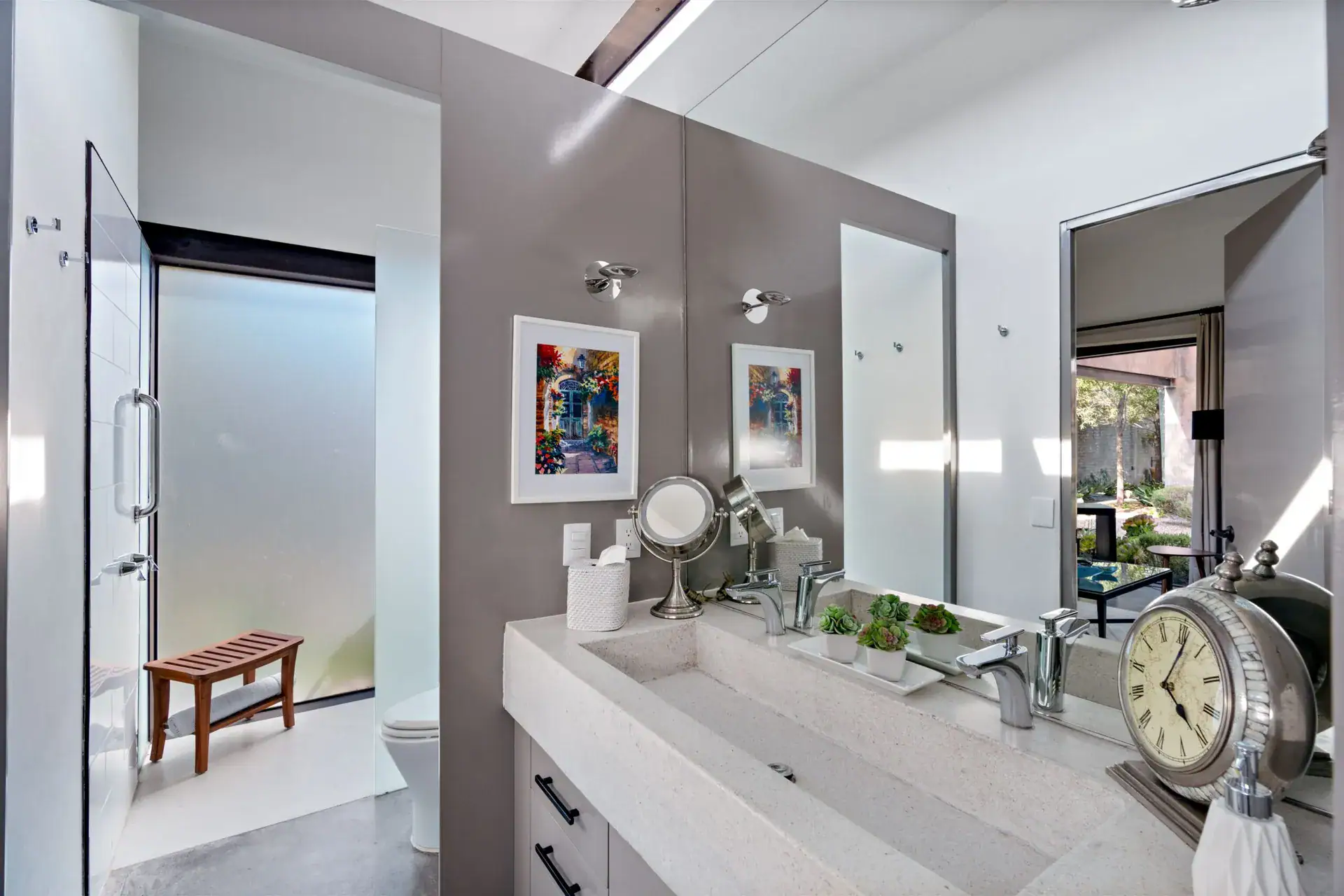 Casa Sanchez Renero, bathroom with a long stone sink, glass shower and colorful framed prints, San Miguel de Allende