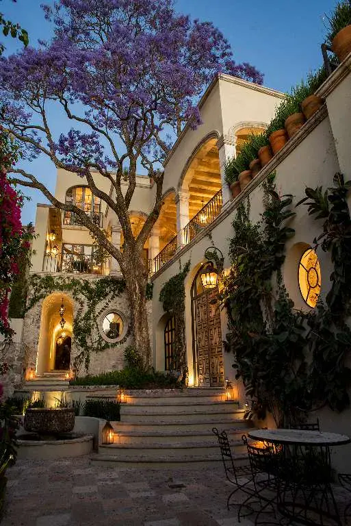 Casa Sereno, pool courtyard at dusk with a jacaranda tree and a stone arch, San Miguel de Allende