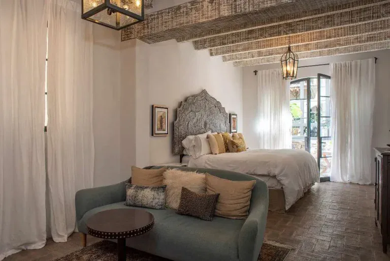 Casa Sereno, primary bedroom with a carved headboard, a green sofa and a beamed ceiling, San Miguel de Allende
