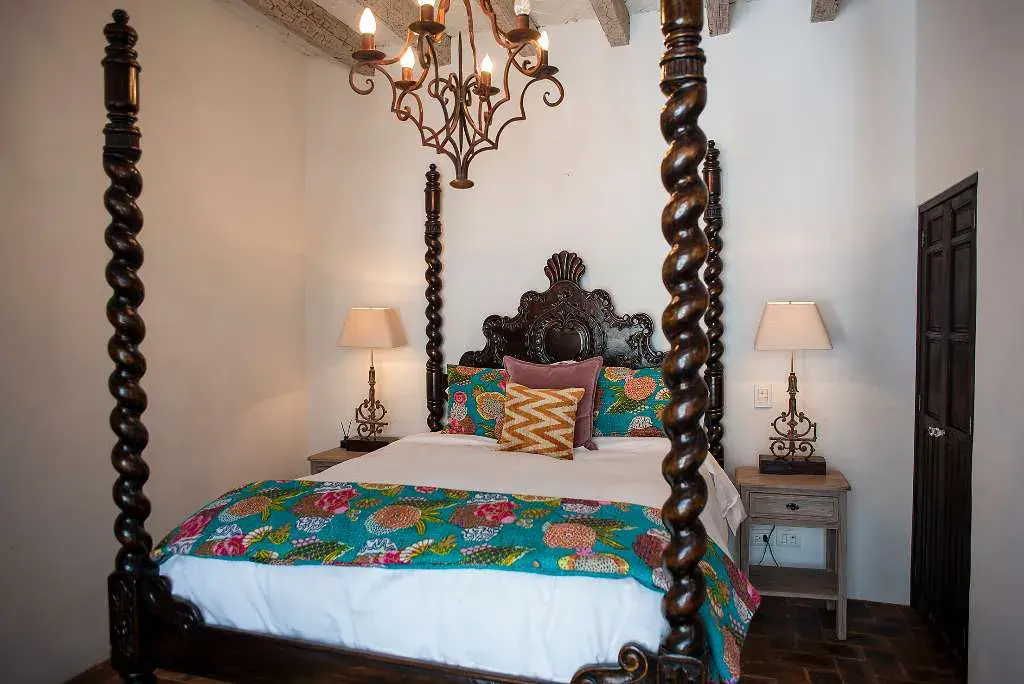 Casa Sereno, bedroom with a carved four-poster bed and a wrought-iron chandelier, San Miguel de Allende