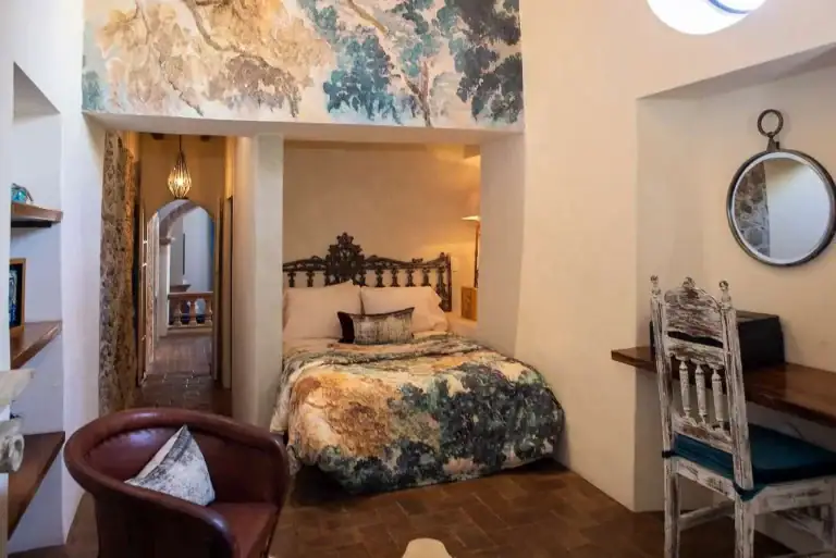 Casa Sereno, bedroom with a painted mural, a carved wood bed and a desk, San Miguel de Allende