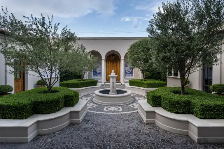 Casa Sienna, courtyard fountain with a mosaic pebble pattern, clipped hedges, olive trees and an arched wooden door, San Miguel de Allende