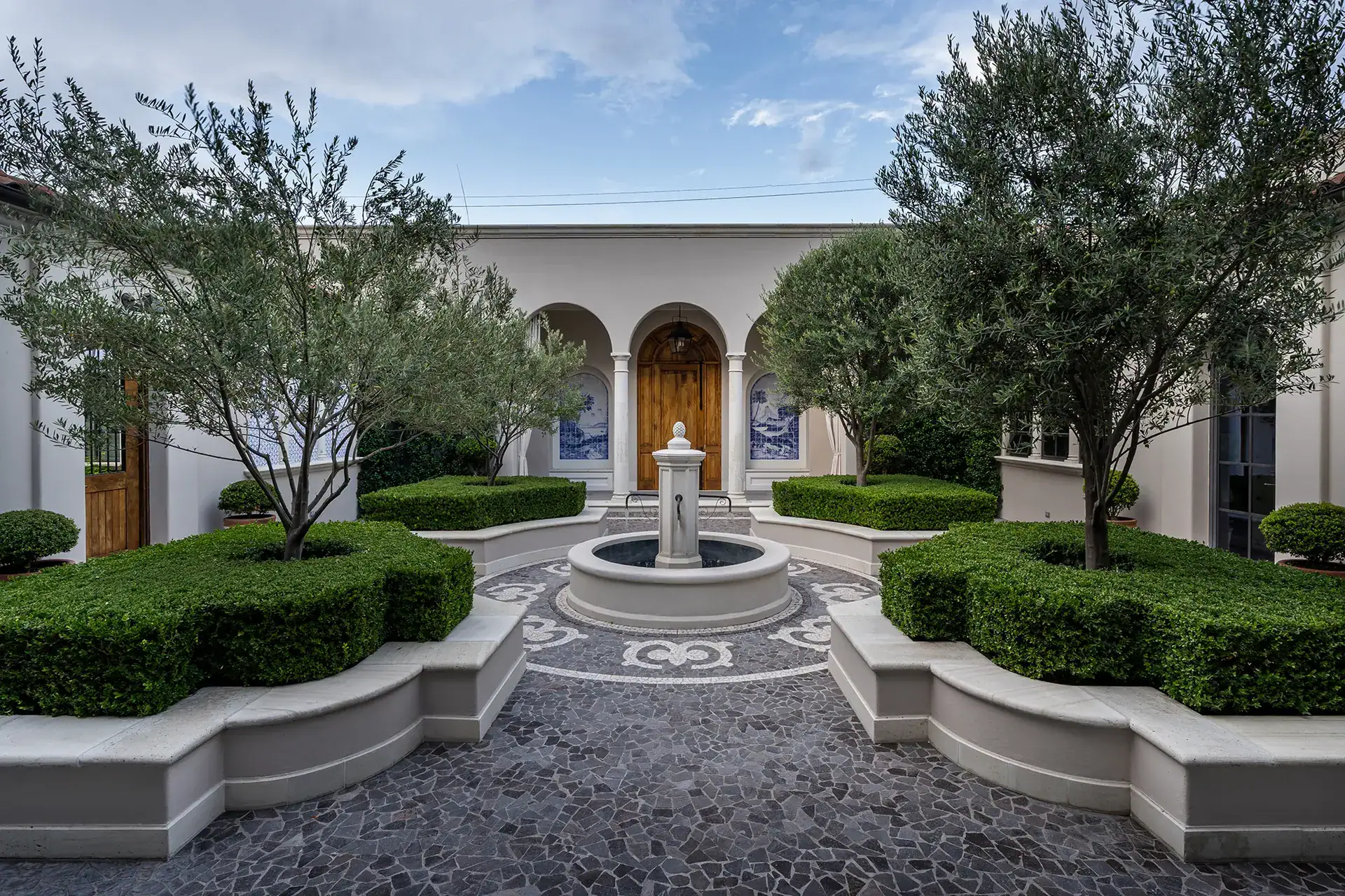 Casa Sienna, courtyard fountain with a mosaic pebble pattern, clipped hedges, olive trees and an arched wooden door, San Miguel de Allende