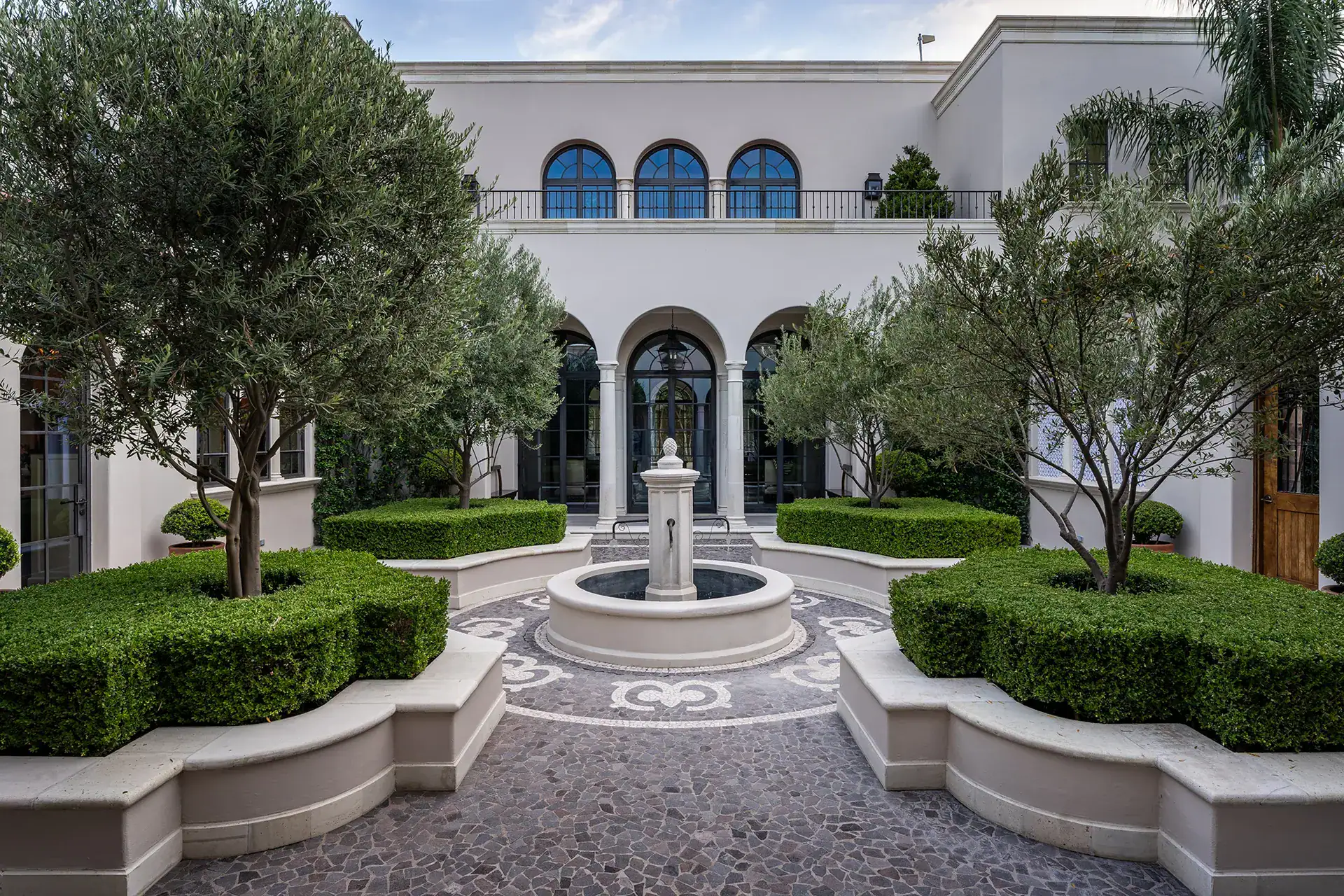 Casa Sienna, two-story courtyard facade with arched windows behind a fountain, hedges and olive trees, San Miguel de Allende