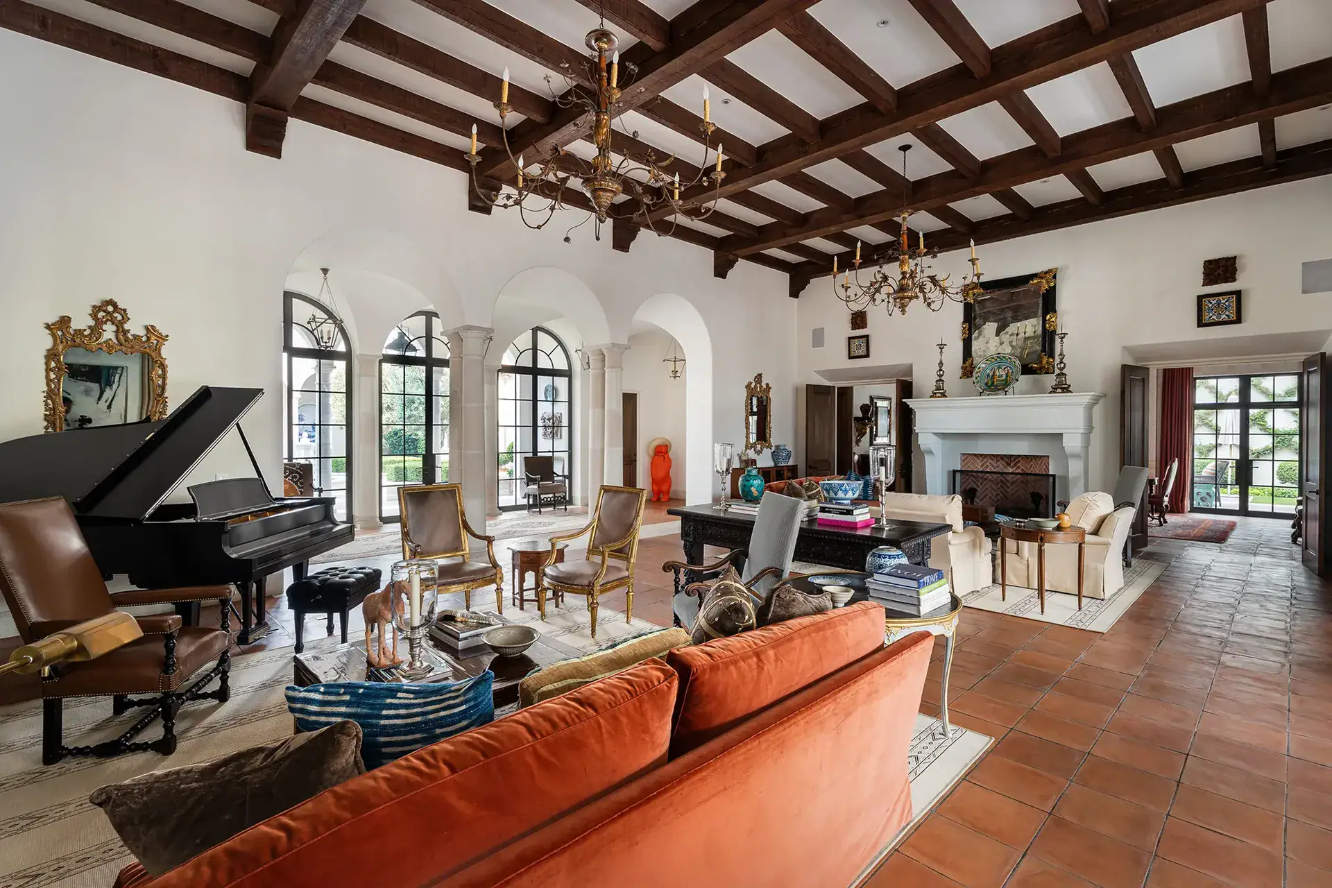 Casa Sienna, living room with a grand piano, rust velvet sofa and a stone fireplace under a beamed ceiling, San Miguel de Allende
