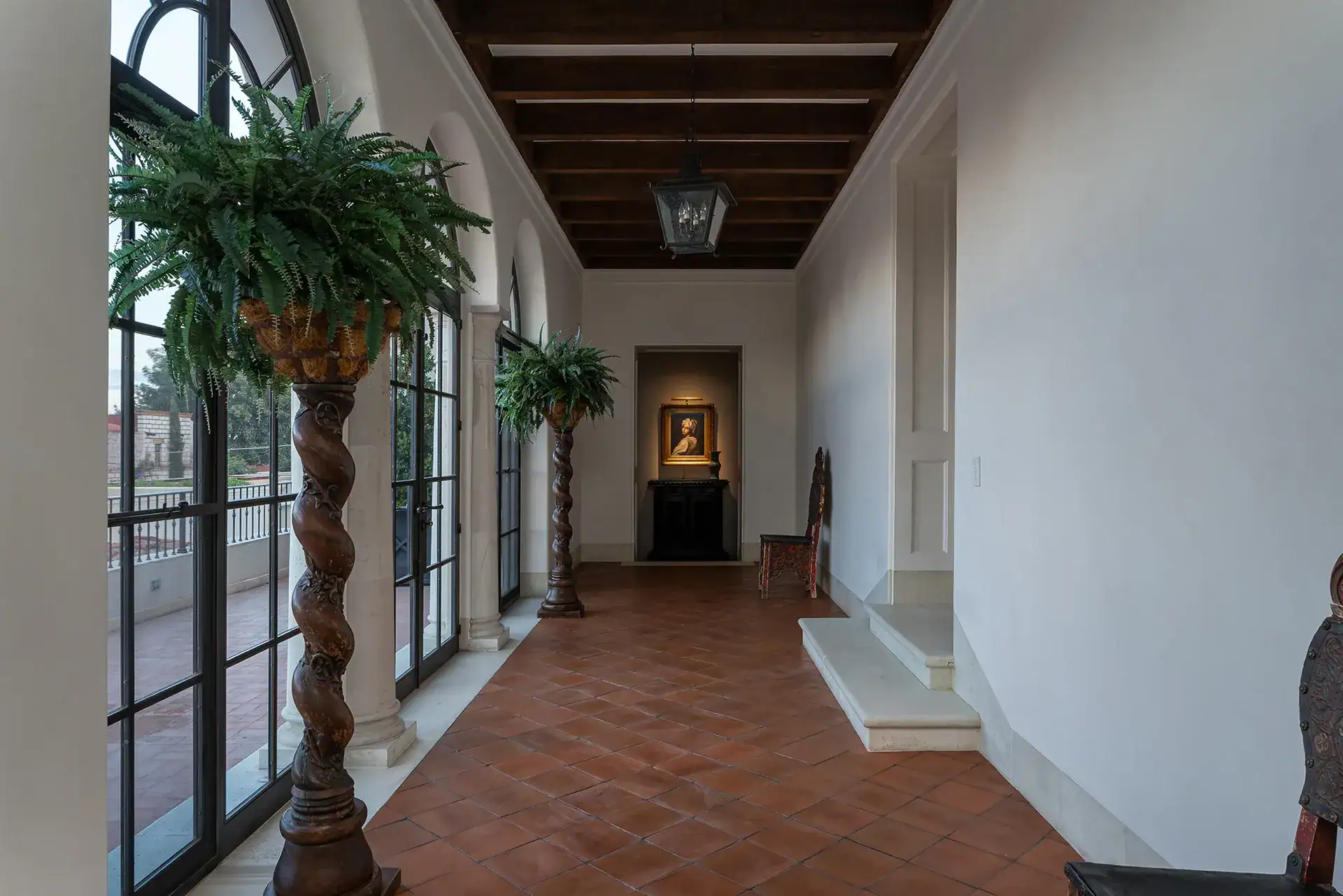 Casa Sienna, upstairs gallery hall with a terracotta floor, arched windows and a potted fern on a carved column, San Miguel de Allende