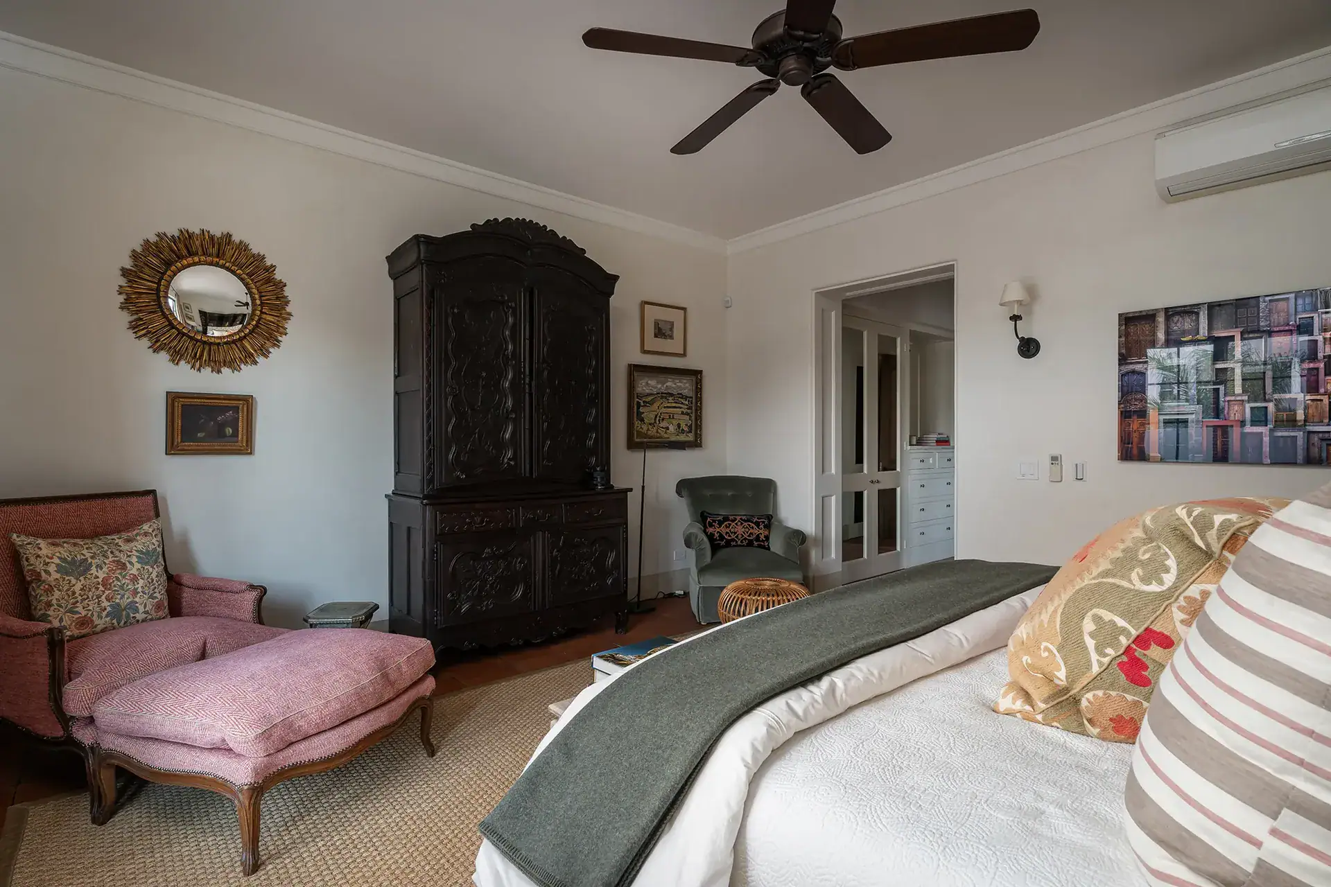 Casa Sienna, bedroom with a pink armchair, carved armoire and ceiling fan, San Miguel de Allende