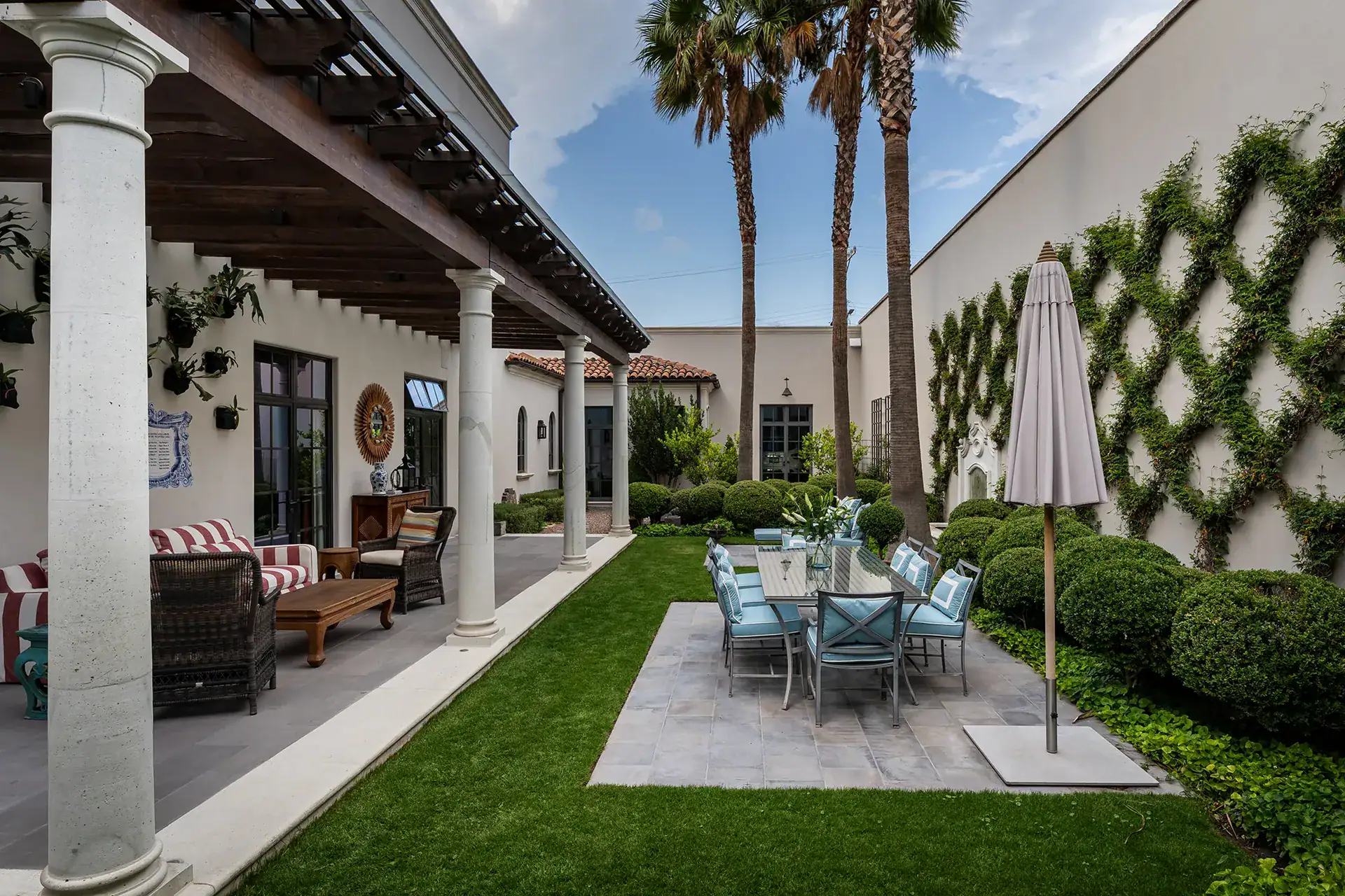 Casa Sienna, covered patio with wicker seating overlooking a lawn, an outdoor dining table and palm trees, San Miguel de Allende