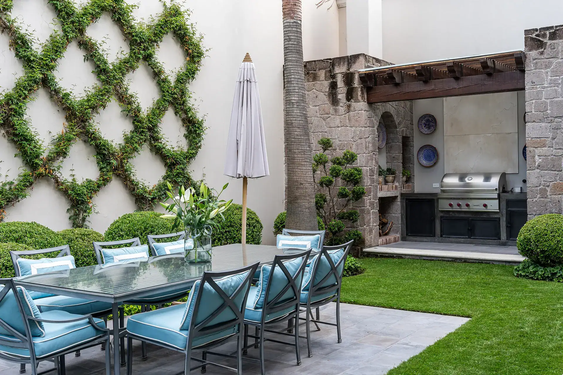 Casa Sienna, outdoor dining table with blue cushioned chairs, a trellised green wall and a built-in grill, San Miguel de Allende