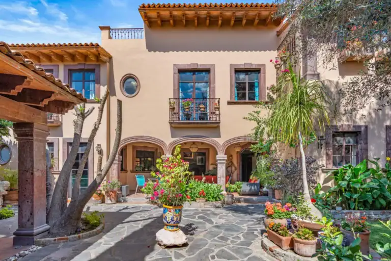 Casa Sirena, courtyard with a flagstone floor, a tall painted urn, bright flowers and a two-story house with an arcade, San Miguel de Allende