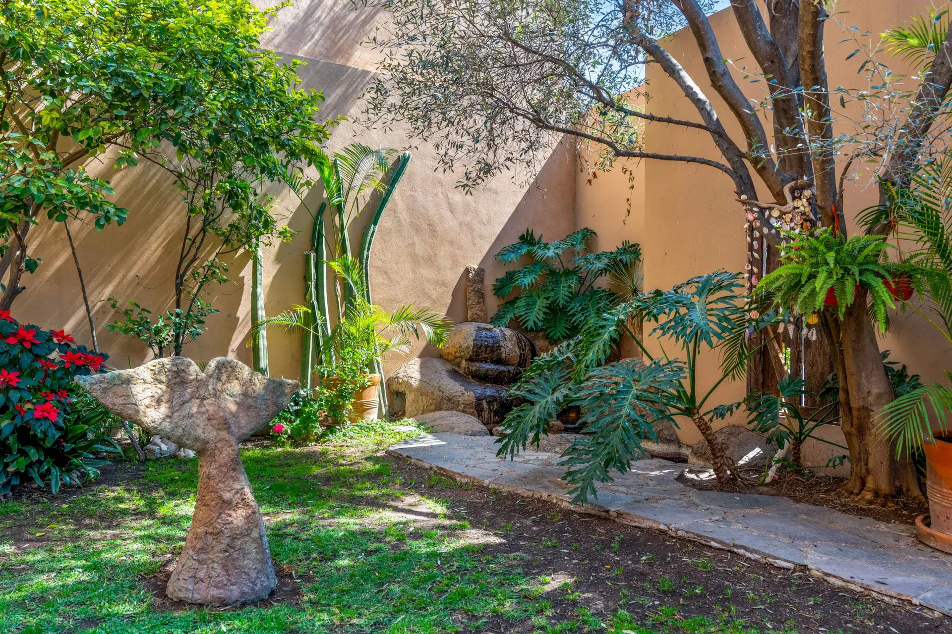 Casa Sirena, garden with a lawn, a mushroom-shaped stone sculpture, a rock waterfall wall and tropical plants, San Miguel de Allende