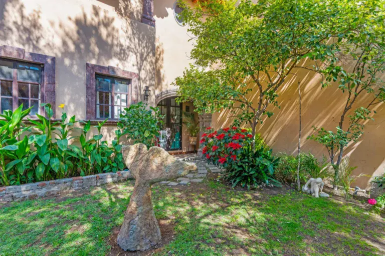 Casa Sirena, lawn with a stone sculpture, flowering plants and the pink house walls and windows, San Miguel de Allende