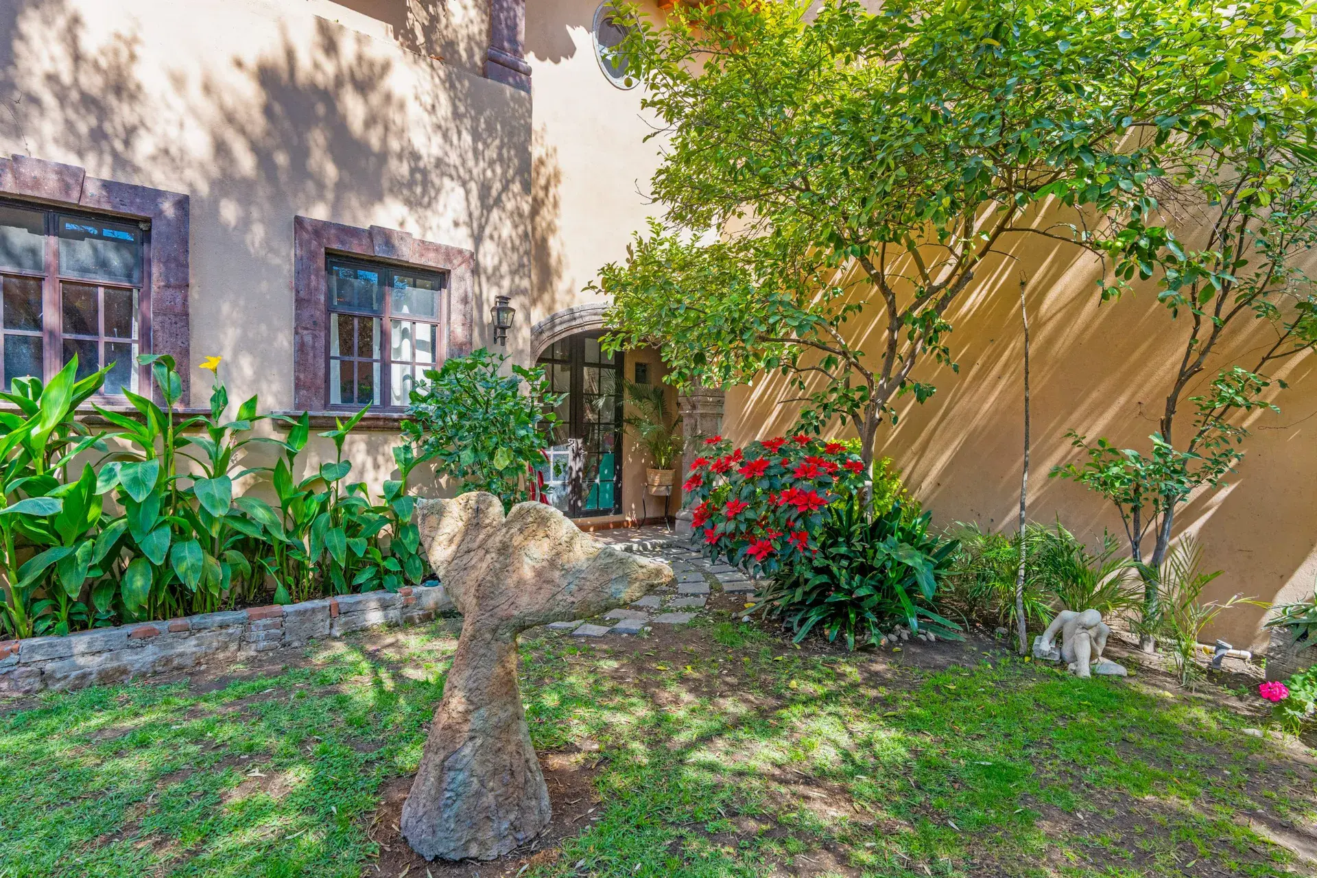 Casa Sirena, lawn with a stone sculpture, flowering plants and the pink house walls and windows, San Miguel de Allende