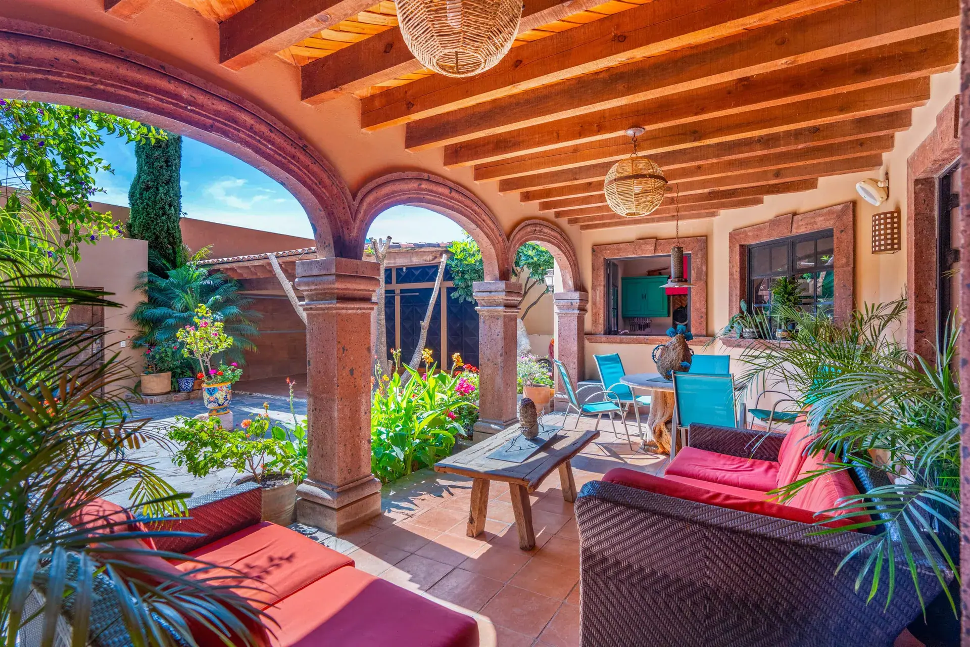 Casa Sirena, covered arcade lounge with arches, a beamed ceiling, a red wicker sofa and a stone coffee table, San Miguel de Allende