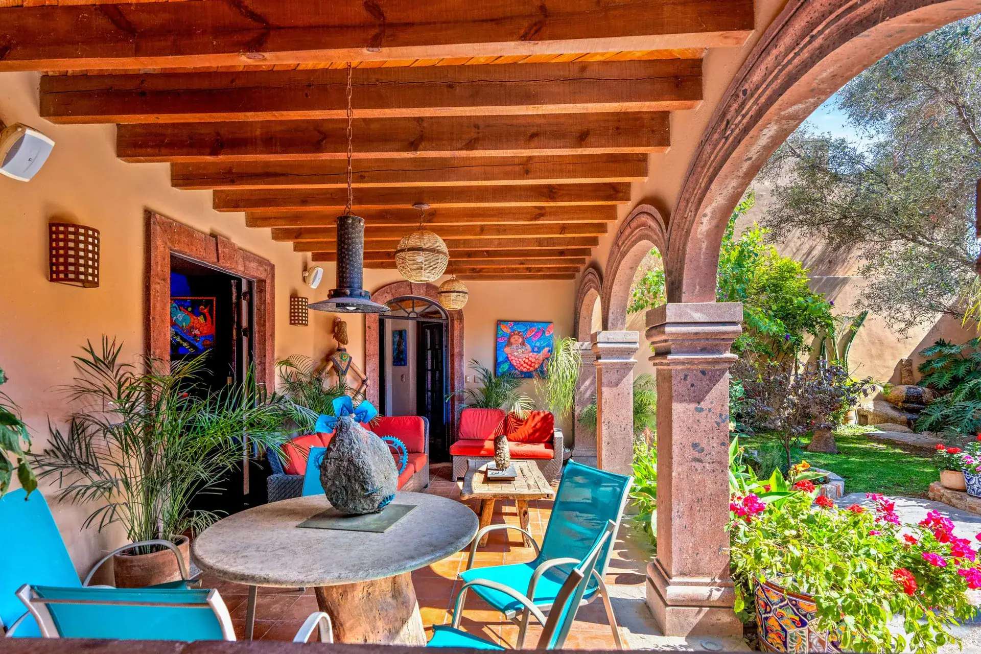 Casa Sirena, arcade seating with a stone round table, turquoise chairs, red cushions and potted palms, San Miguel de Allende