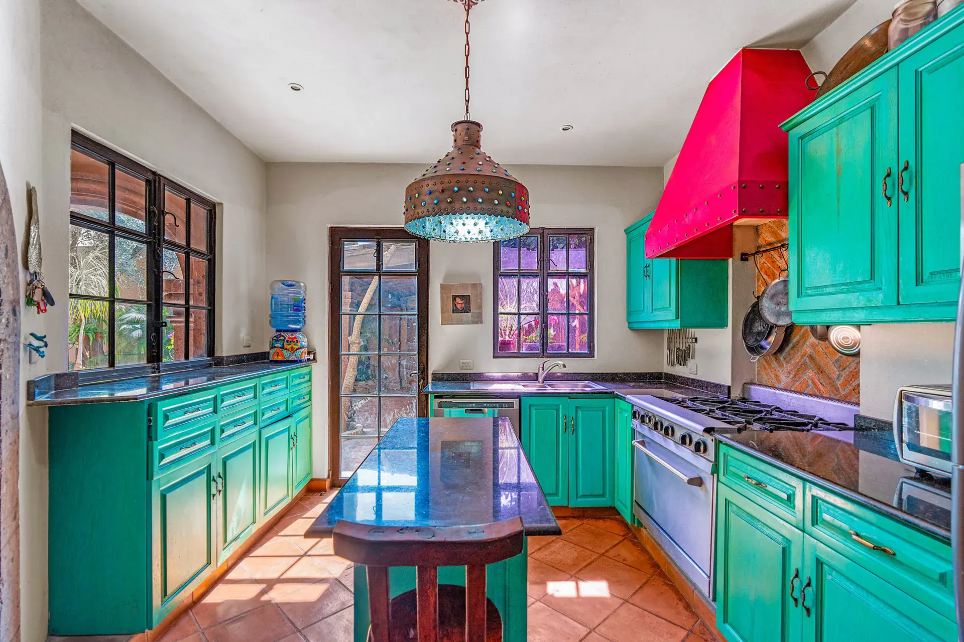 Casa Sirena, kitchen with turquoise cabinets, a granite island, a pendant light and glass doors to the garden, San Miguel de Allende
