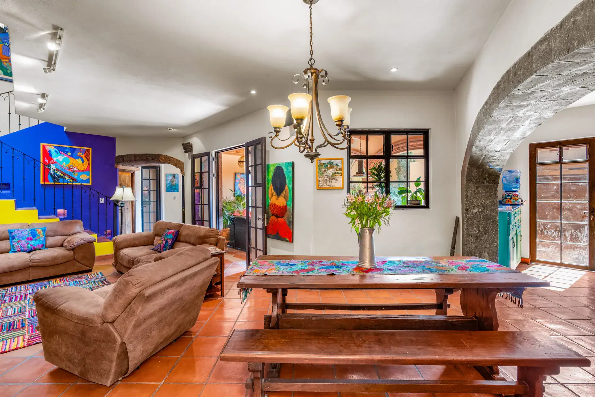 Casa Sirena, living room with brown sofas, a long wood table with benches, a bright staircase and colorful paintings, San Miguel de Allende