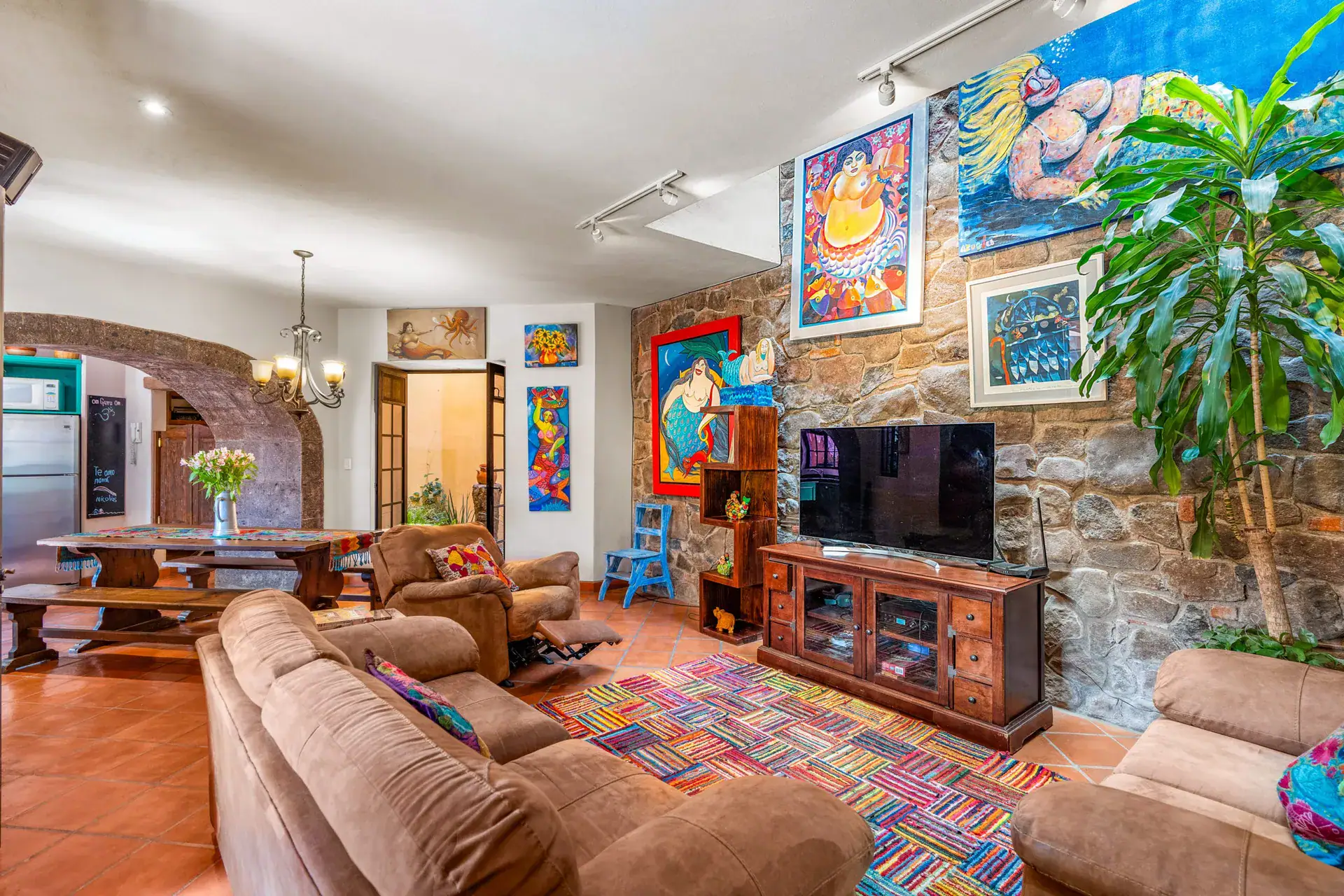 Casa Sirena, living room with a stone feature wall, a television and a view to the dining table and kitchen, San Miguel de Allende