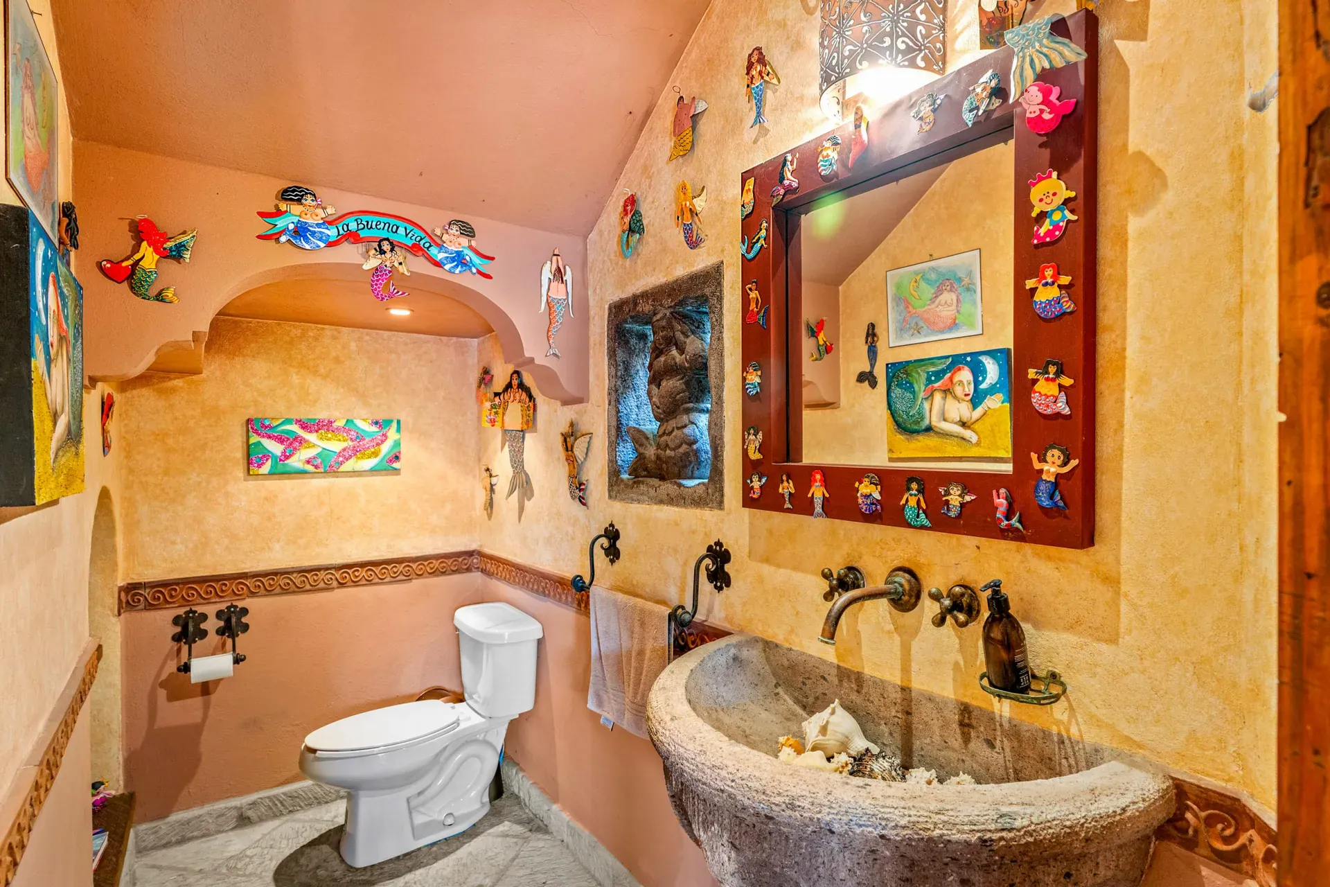 Casa Sirena, powder room with a yellow wall, a carved stone sink, a decorated mirror and a painted shell mural, San Miguel de Allende