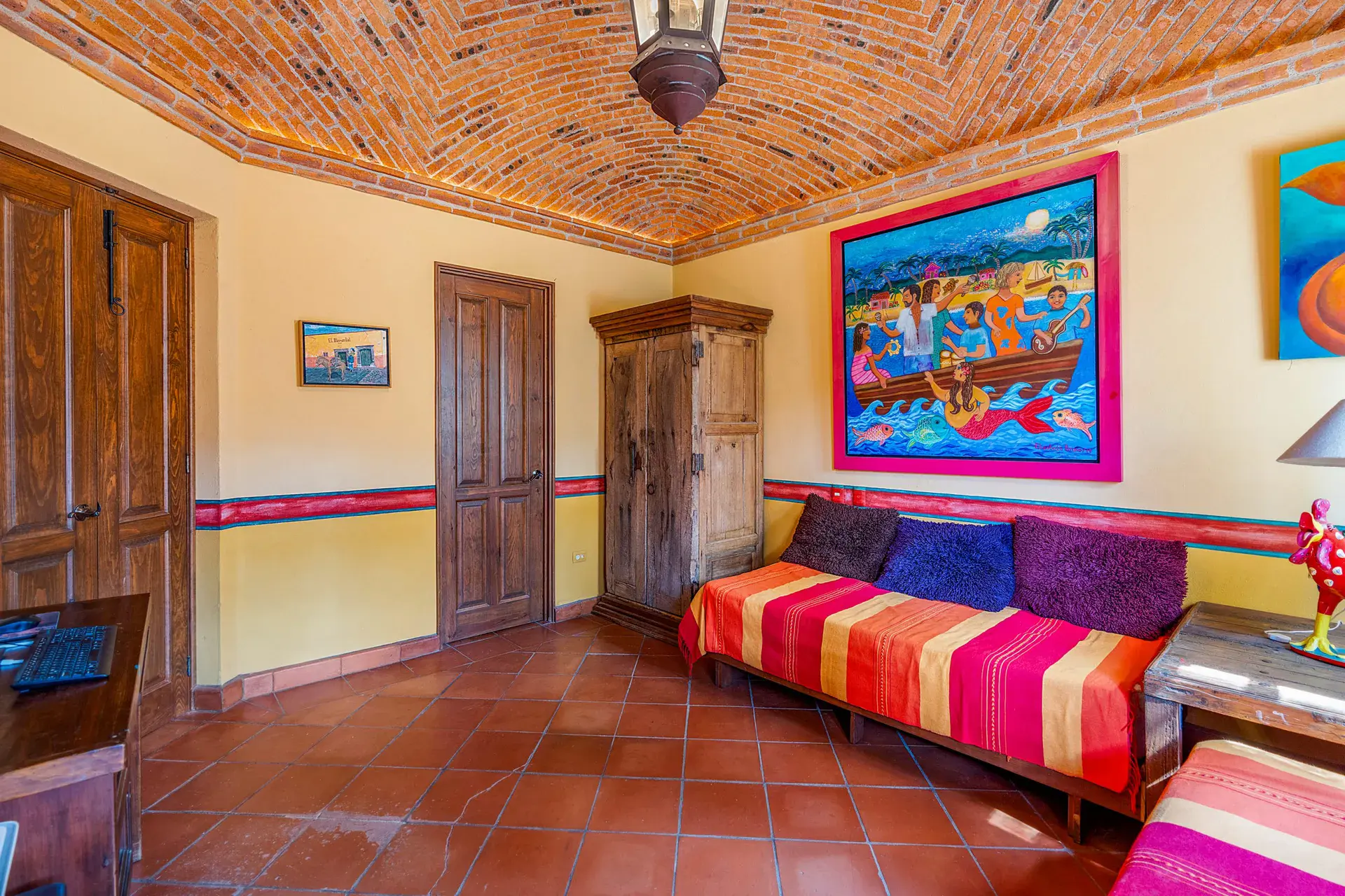 Casa Sirena, sitting room with a brick vaulted ceiling, a striped daybed, a large painting of boats and a wood armoire, San Miguel de Allende