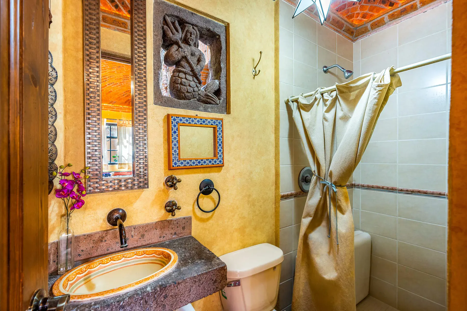 Casa Sirena, bathroom with a gold vanity, a round basin, a mirror with a carved relief and a shower curtain, San Miguel de Allende