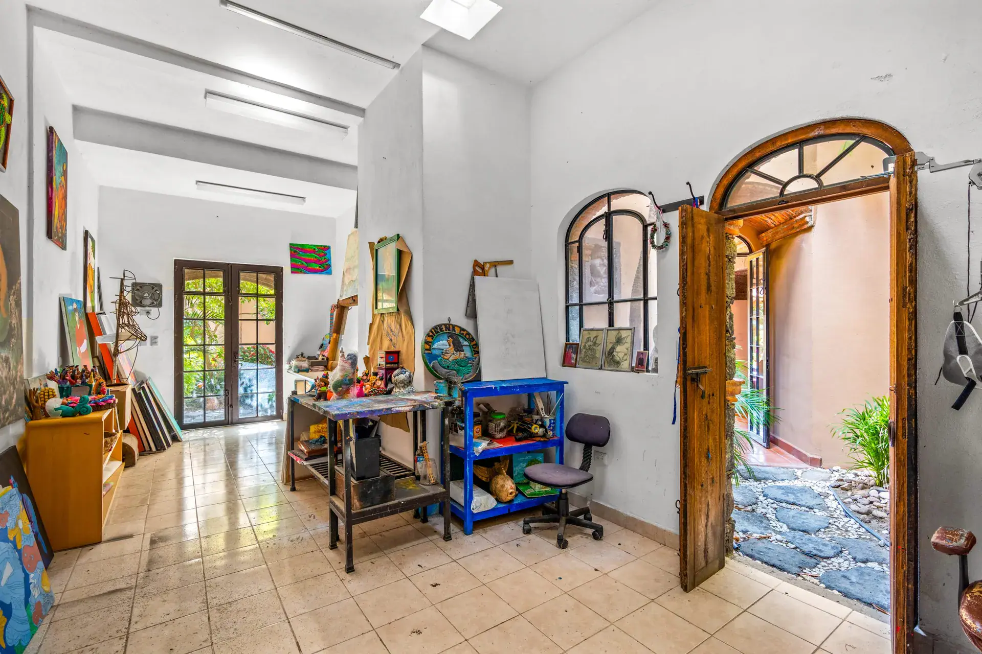 Casa Sirena, artist studio with a worktable, paintings, a tiled floor and an arched wood door to the courtyard, San Miguel de Allende