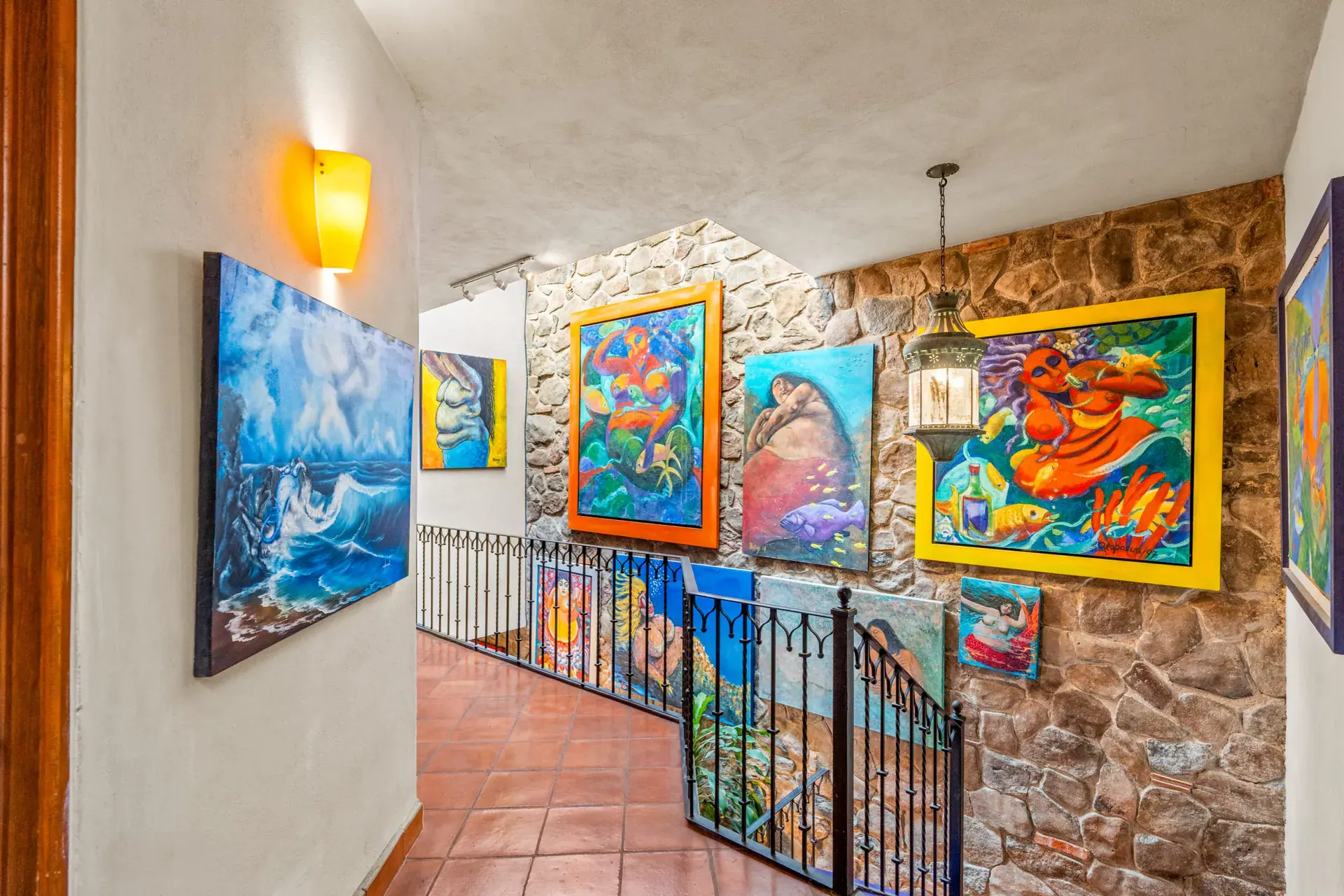 Casa Sirena, stair landing with a stone wall, an iron railing and large colorful paintings, San Miguel de Allende