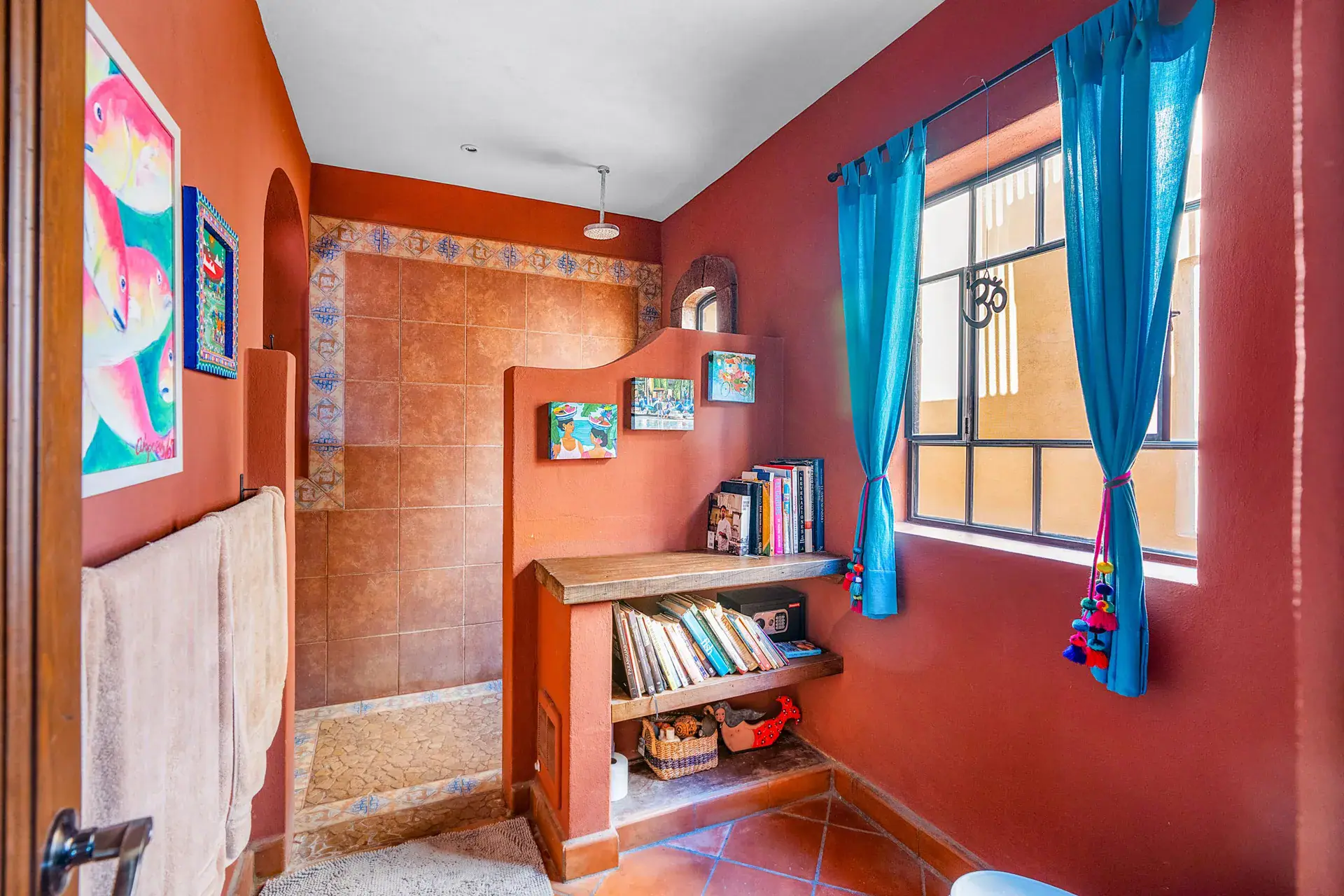 Casa Sirena, bathroom with a deep red wall, a tiled shower, a bookshelf and turquoise curtains, San Miguel de Allende