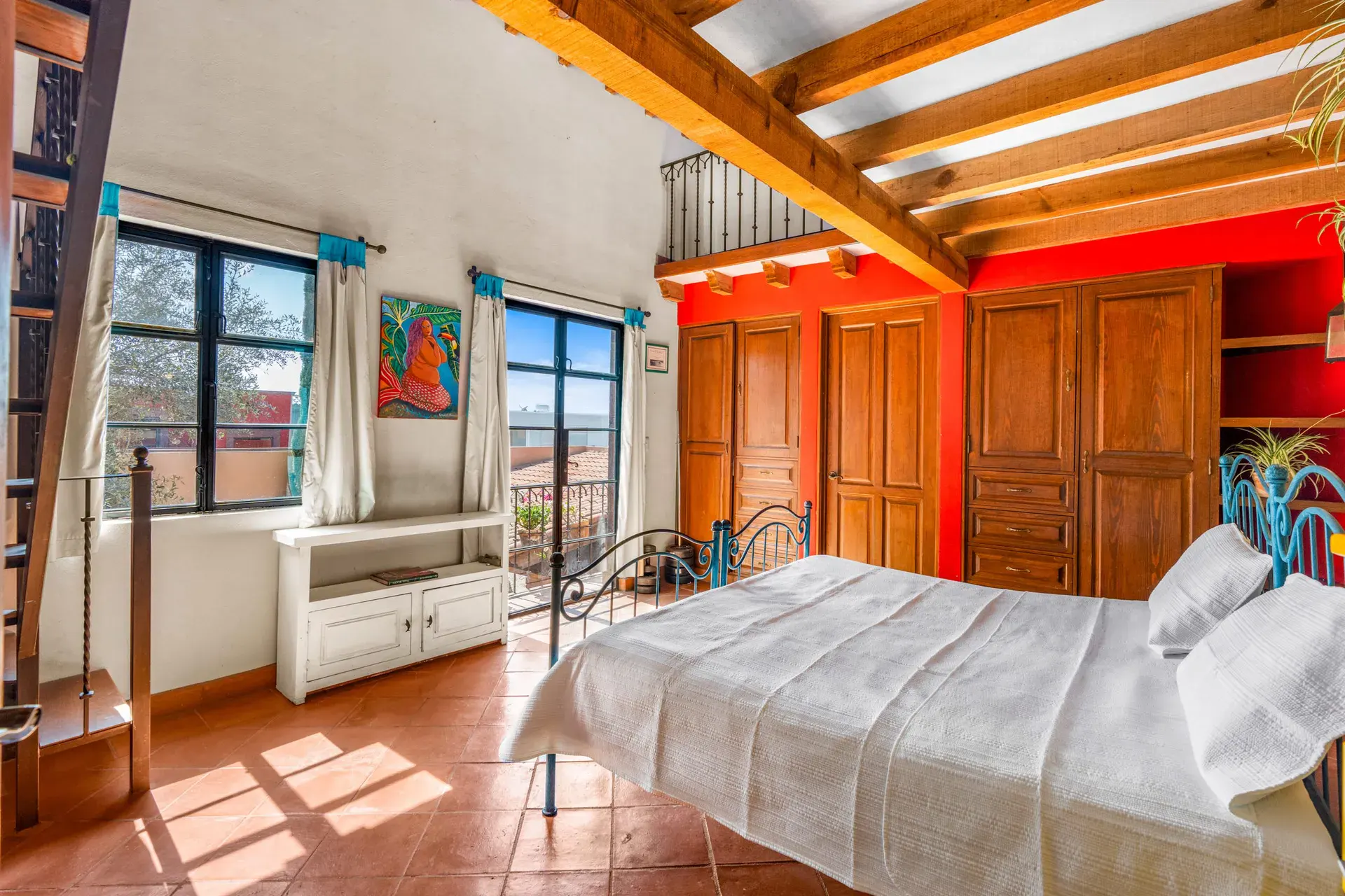 Casa Sirena, loft bedroom with an iron bed, a red wardrobe wall, a white window bench and a beamed ceiling, San Miguel de Allende