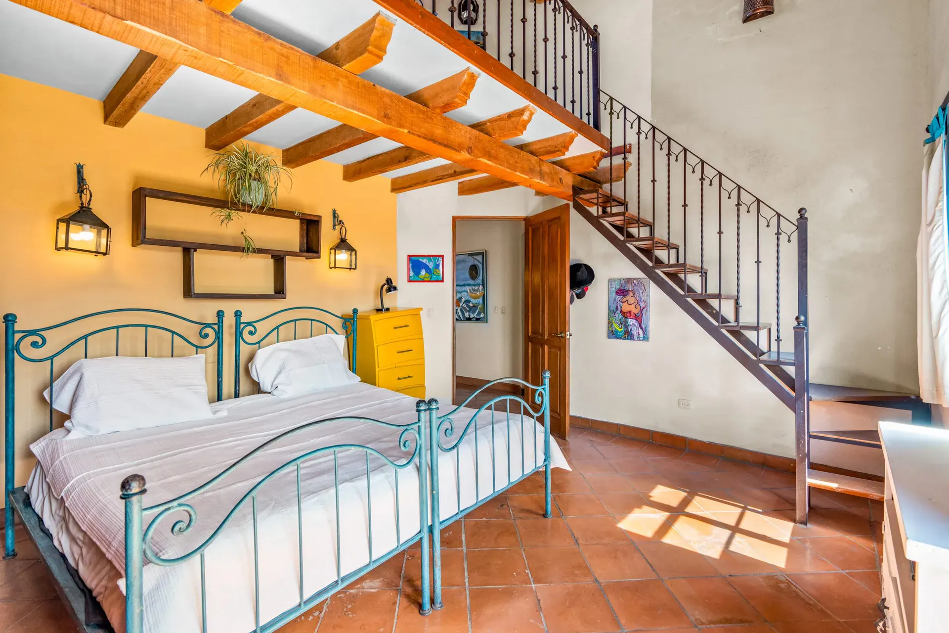 Casa Sirena, bedroom with two iron beds, a yellow chest, a spiral stair to a loft and beams, San Miguel de Allende