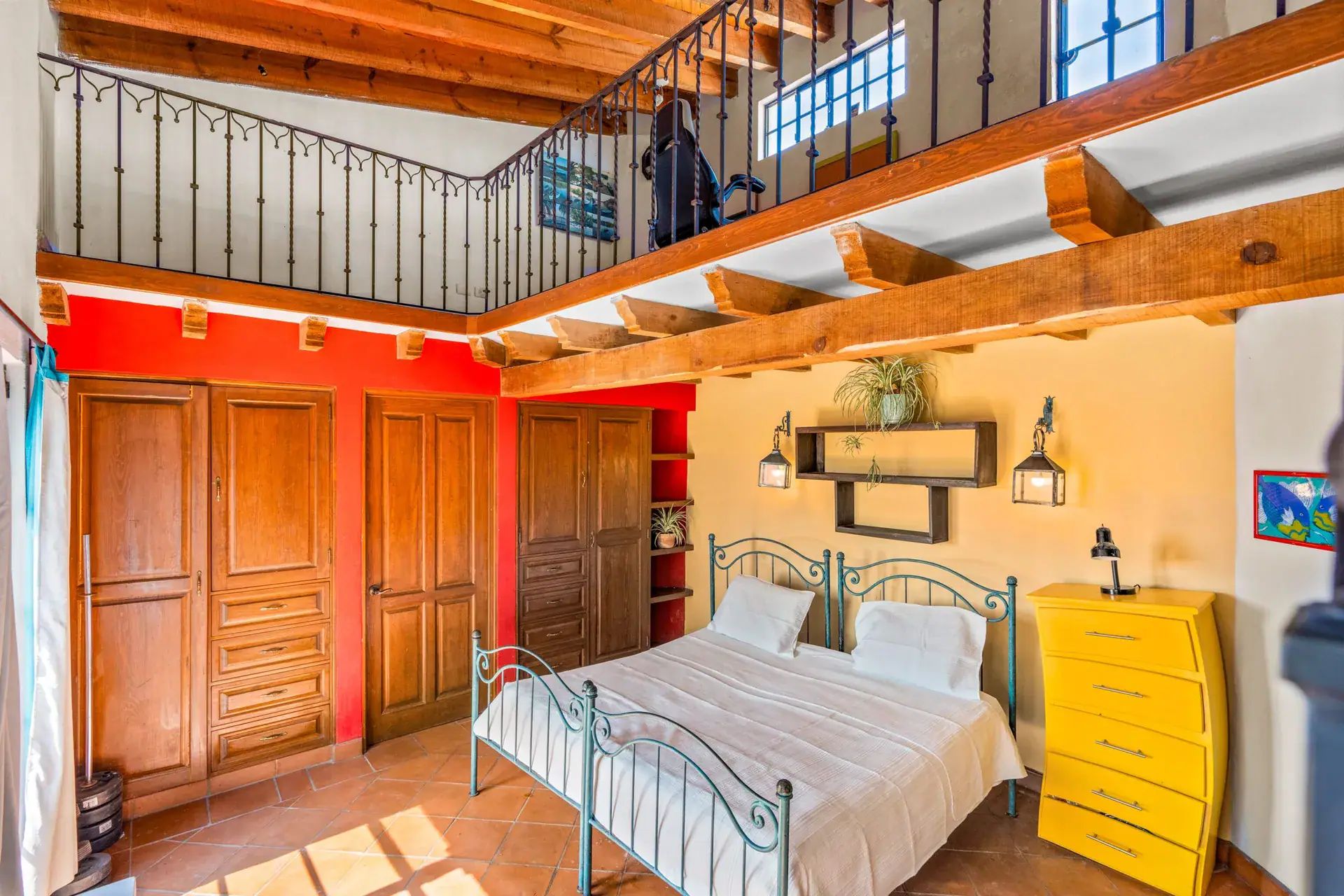 Casa Sirena, loft bedroom with an iron bed, a red wardrobe wall, a yellow dresser and an iron railing above, San Miguel de Allende