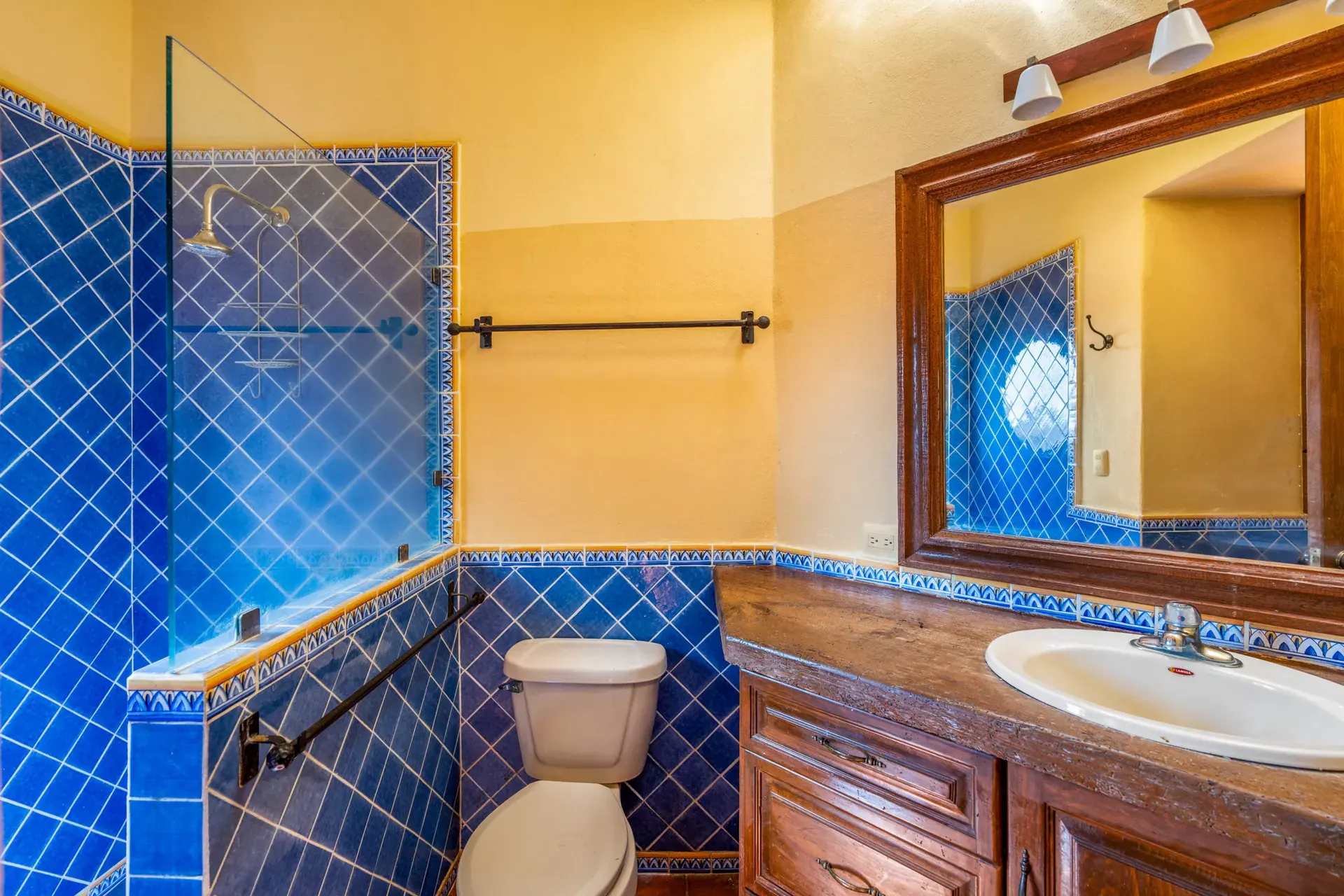 Casa Sirena, bathroom with blue tile, a yellow wall, a large mirror and a wood vanity, San Miguel de Allende