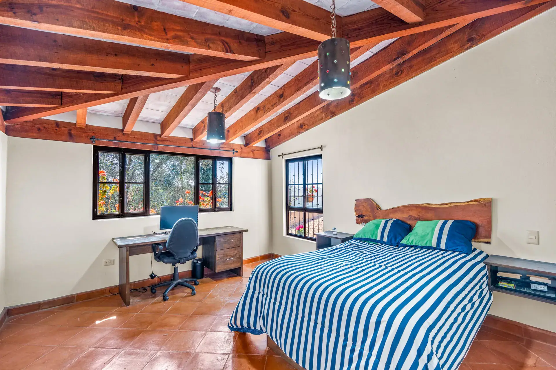 Casa Sirena, bedroom with a blue striped bedspread, a desk and a computer chair under a timber ceiling, San Miguel de Allende