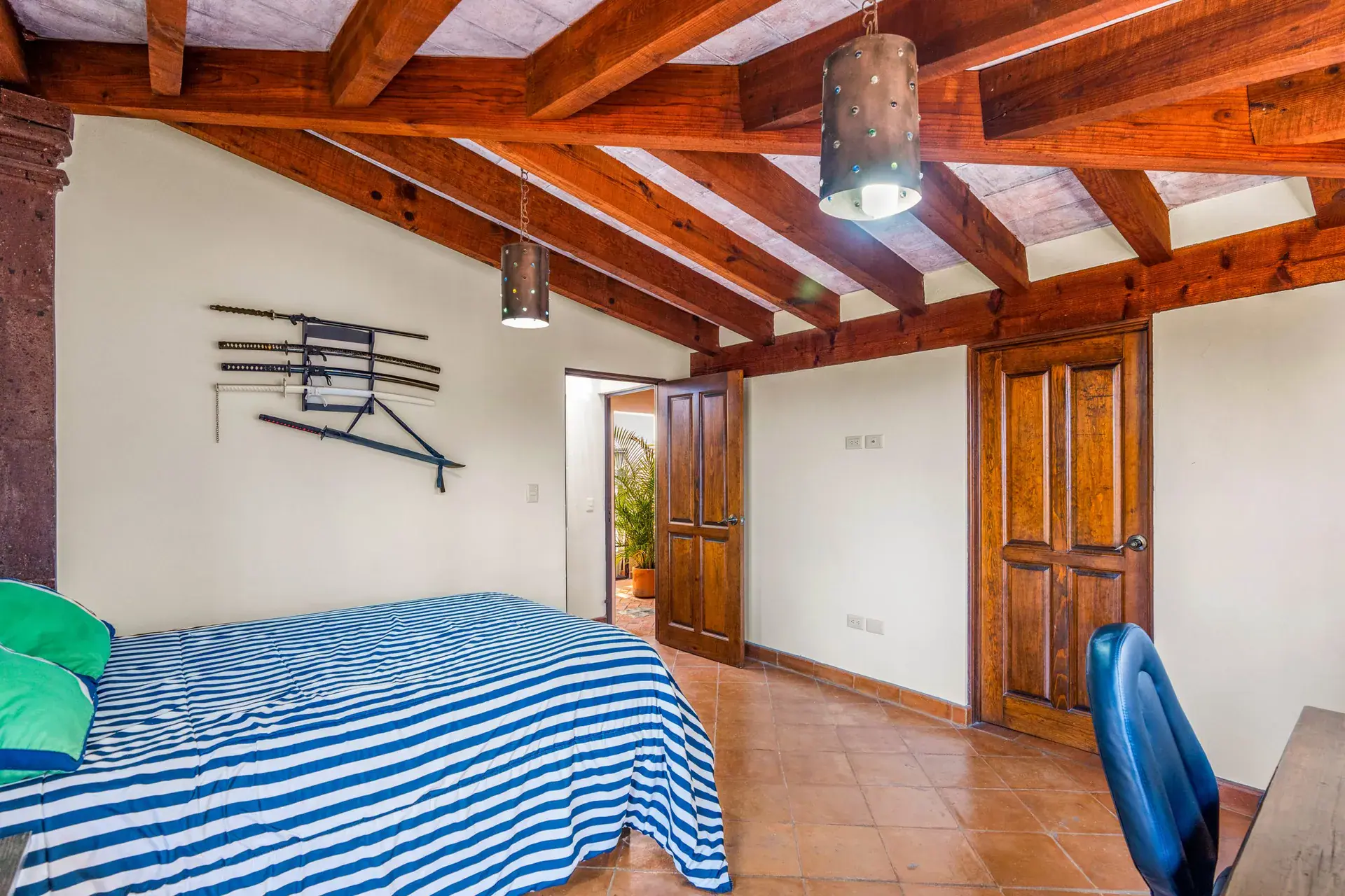 Casa Sirena, bedroom with a blue and white striped bed, an office chair and a timber ceiling, San Miguel de Allende
