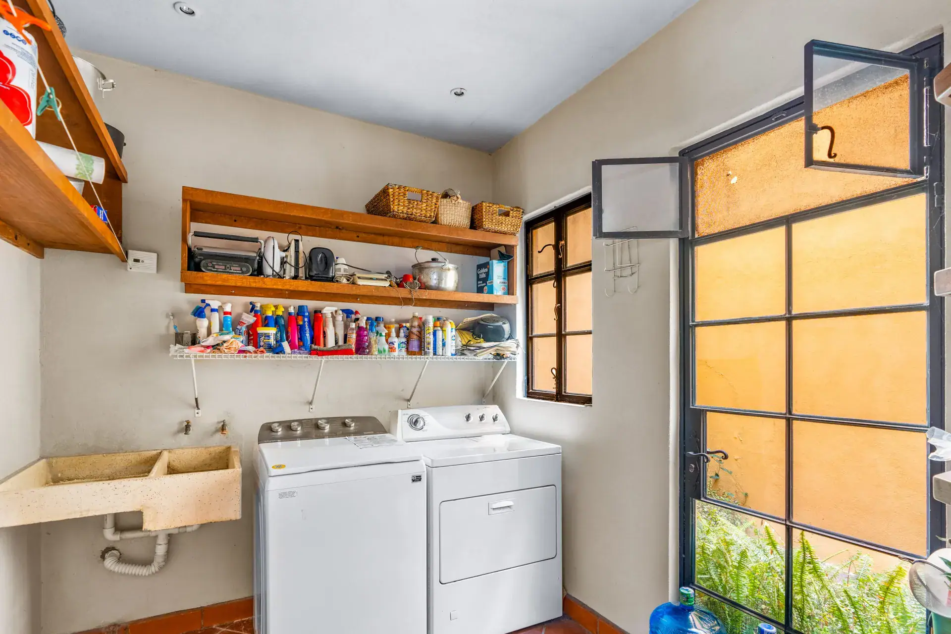 Casa Sirena, laundry room with a washer and dryer, a stone sink, a shelf of supplies and a glass door, San Miguel de Allende