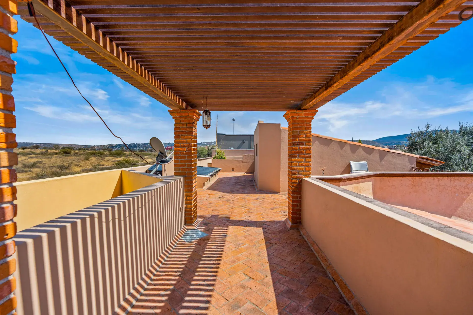 Casa Sirena, rooftop walkway with a brick herringbone floor, a pergola and a view of the golf course hills, San Miguel de Allende
